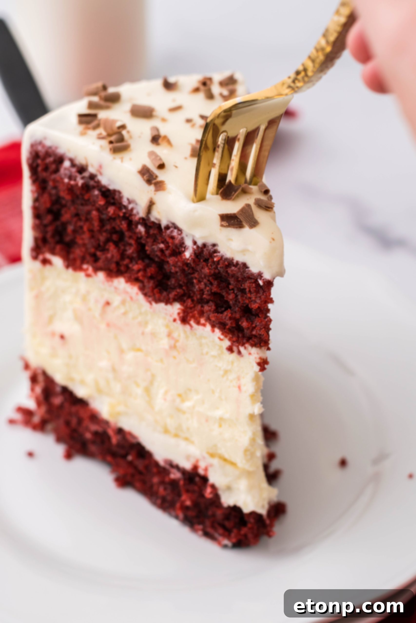 A fork taking a bite from a slice of Red Velvet Cheesecake Cake, highlighting its moistness and layers.