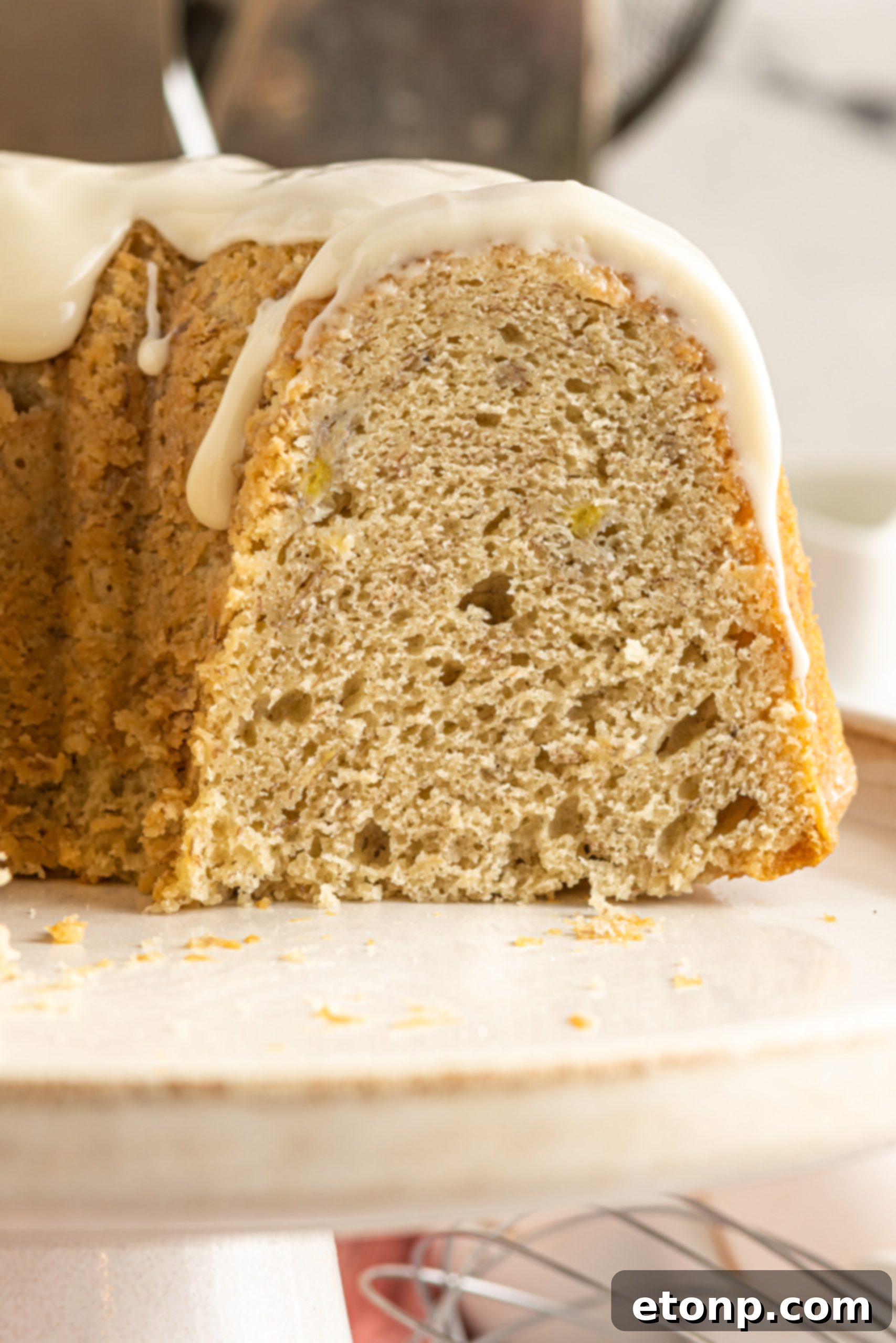 Banana Cake covered in sour cream frosting on a cake stand sliced