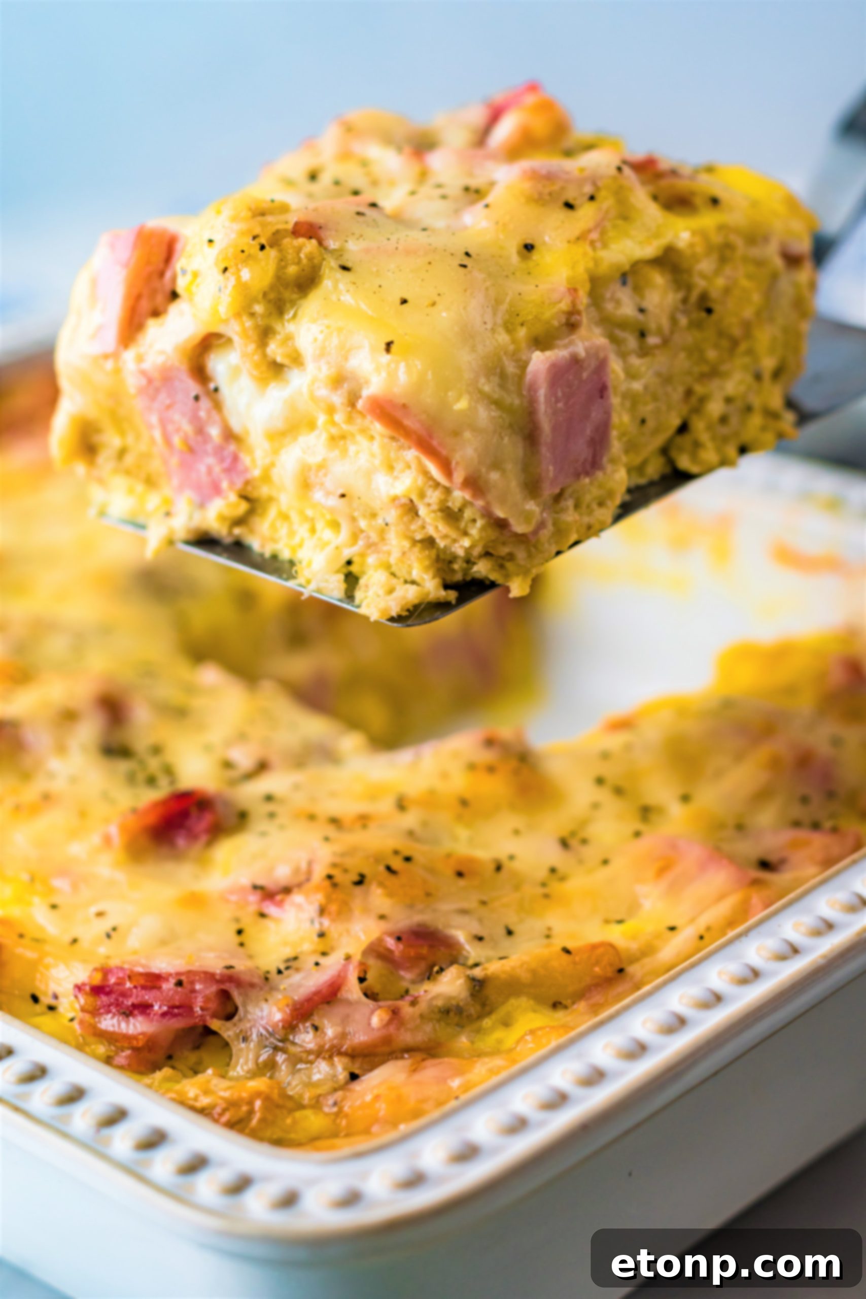 Eggs Benedict in a white casserole dish with a slice being lifted out on a spatula