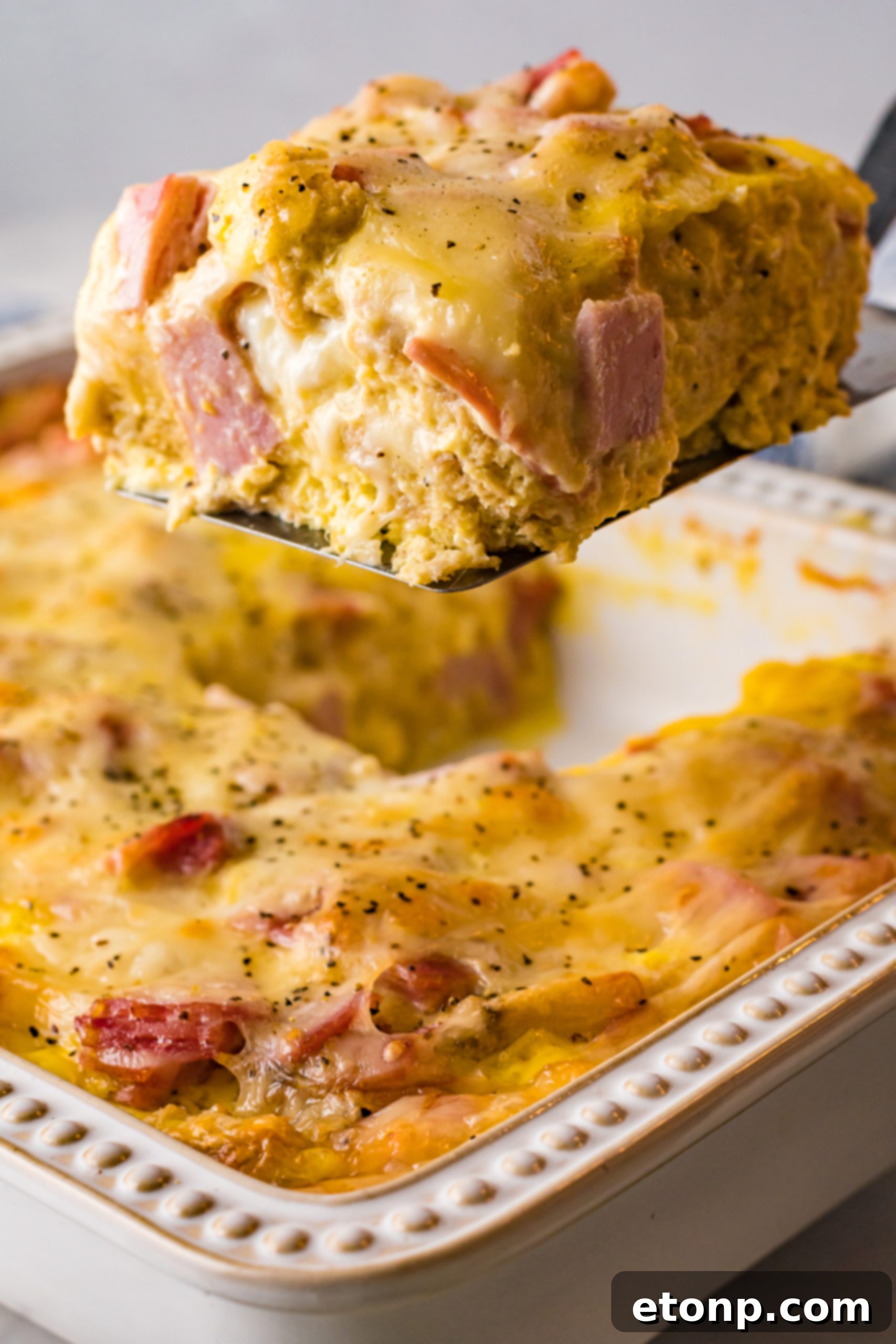 Eggs Benedict in a white casserole dish with a slice being lifted out on a black spatula