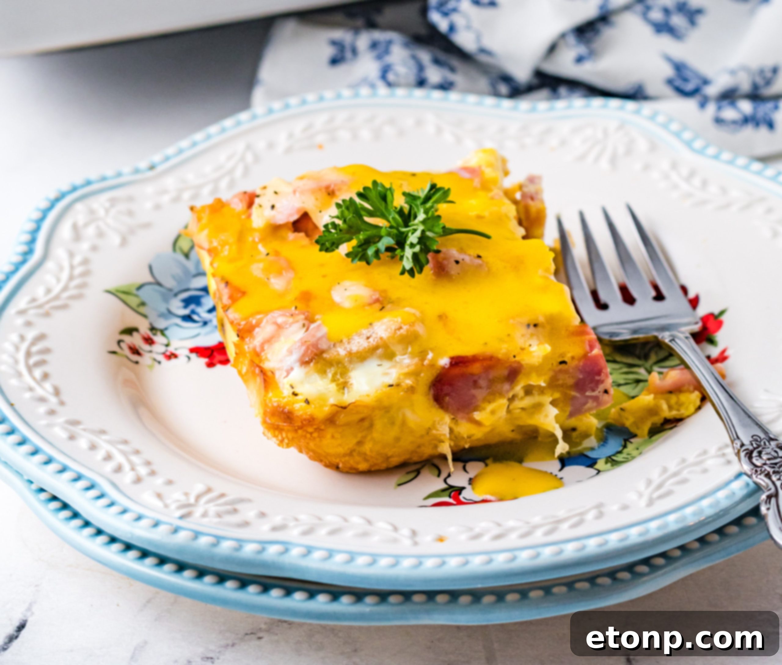 Eggs Benedict on a white plate with blue trim with a fork next to the slice
