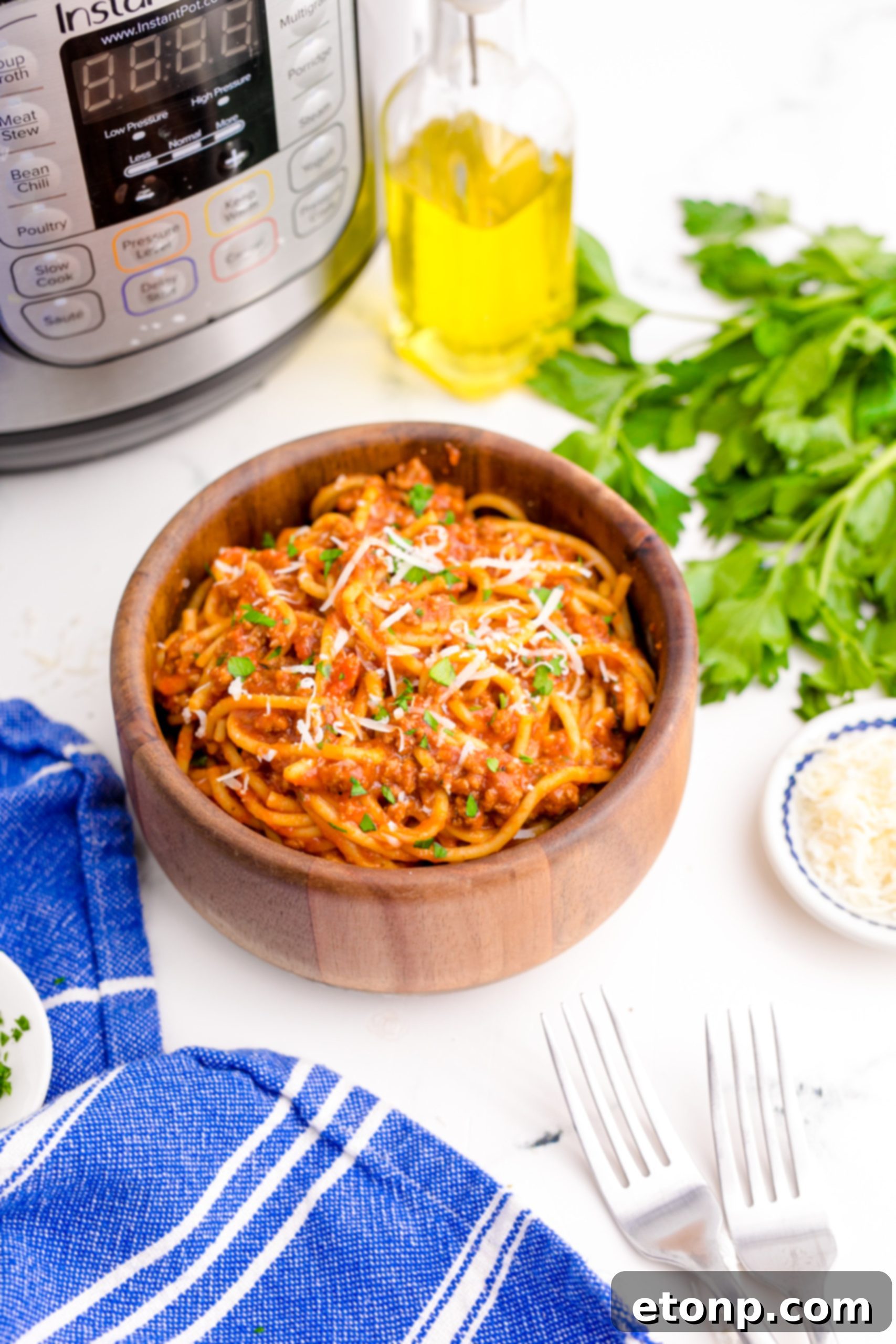 One-Pot Instant Pot Spaghetti 12 Instant Pot Spaghetti in a wooden bowl with a blue napkin, fork, Instant Pot, and a small bowl of Parmesan cheese in the background