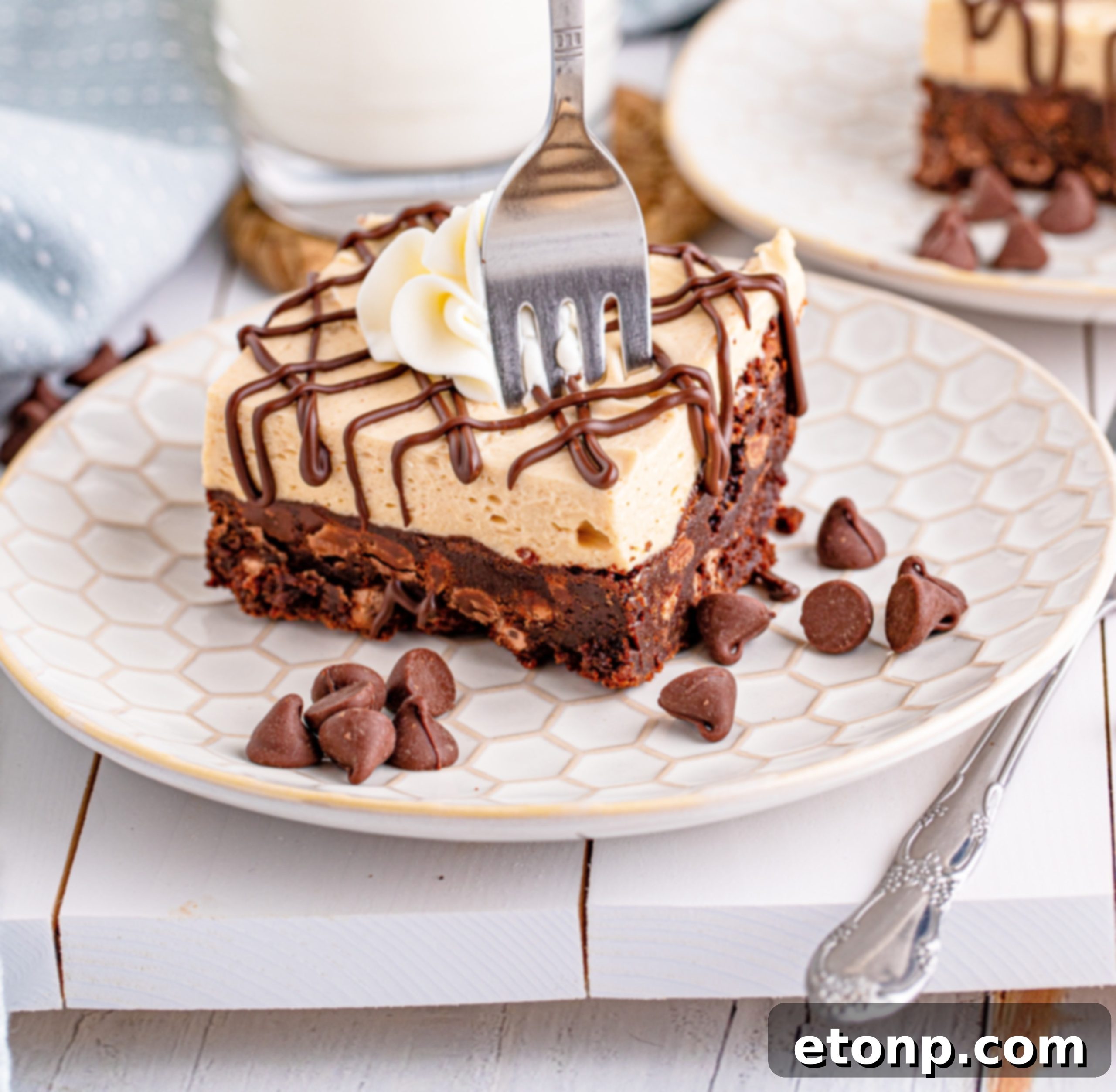 Peanut Butter Brownies on a white plate drizzled with chocolate and topped with whipped cream with a fork going through the brownie
