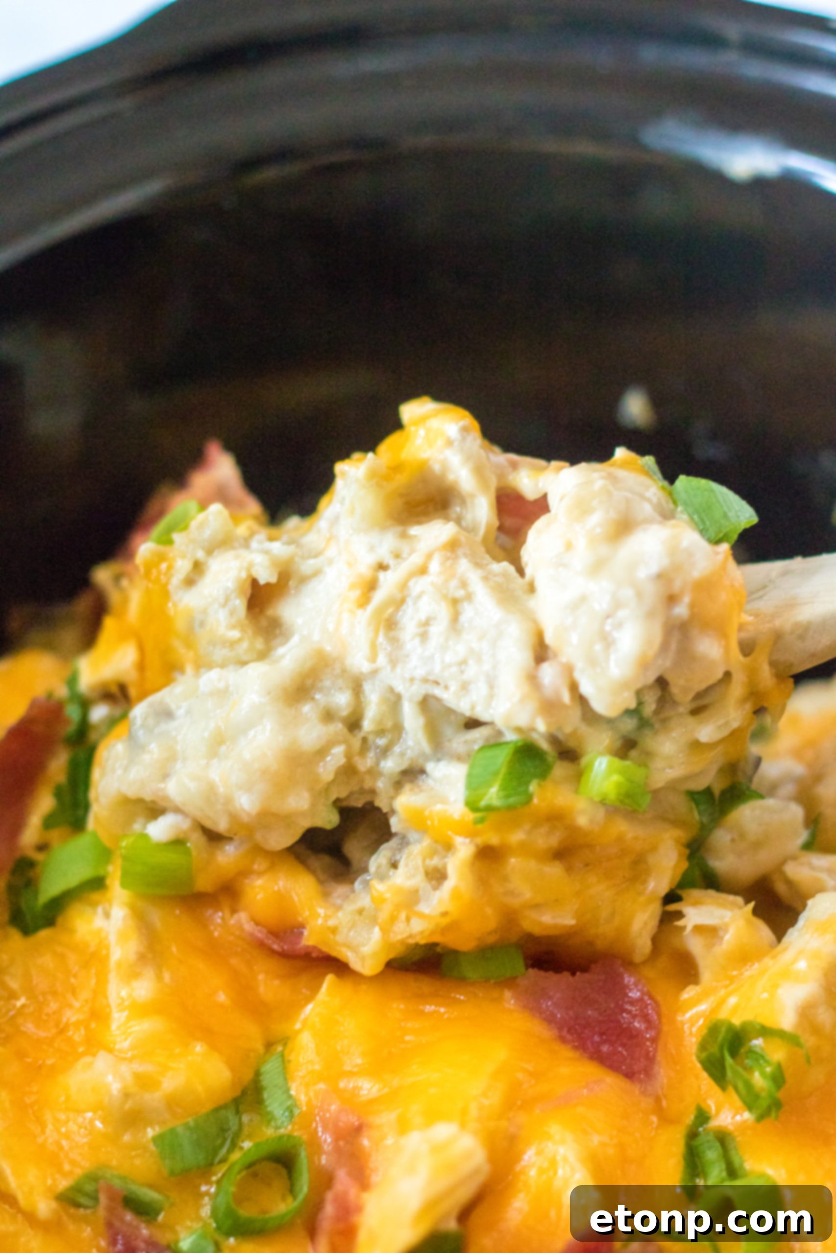 slow cooker photo of a spoon lifting the chicken covered in cheese and tater tots