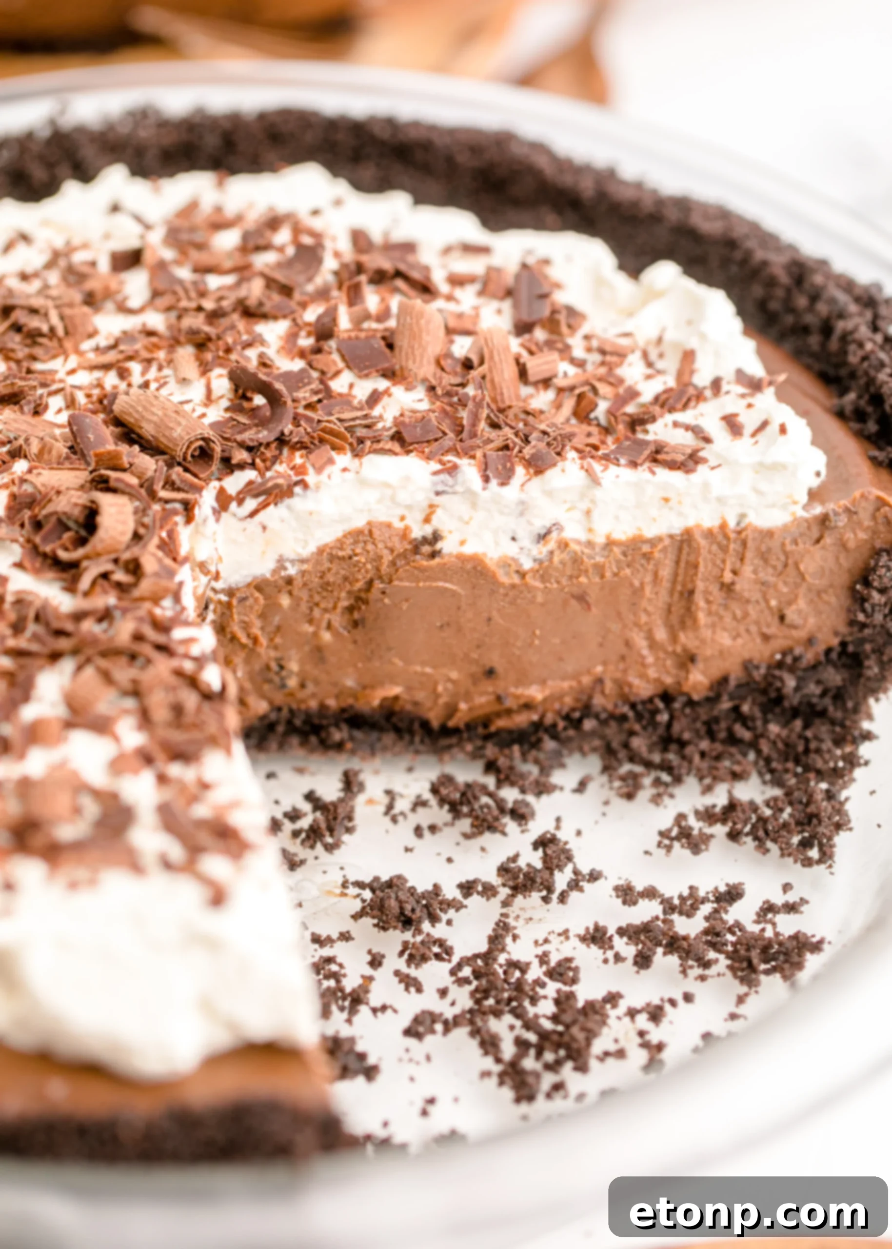 Chocolate Cream Pie topped with whipped cream and chocolate shavings on a white pie dish with a slice cut out, ready to be served