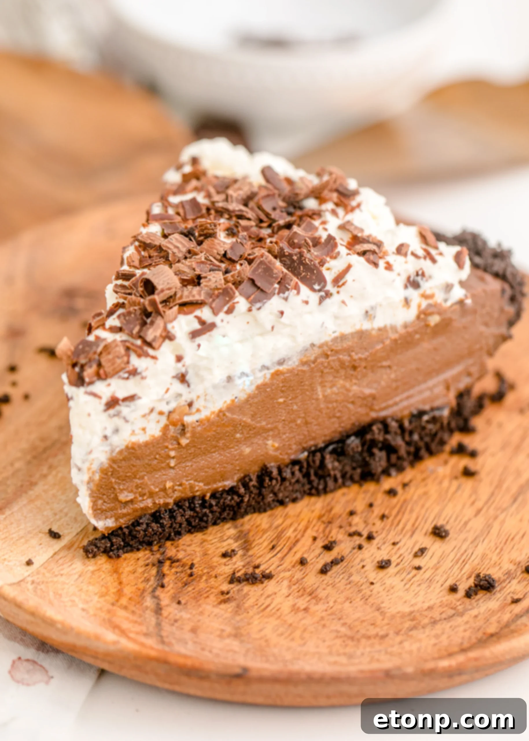 Chocolate Cream Pie topped with whipped cream and chocolate shavings on a brown wooden cutting board, showcasing its rustic elegance