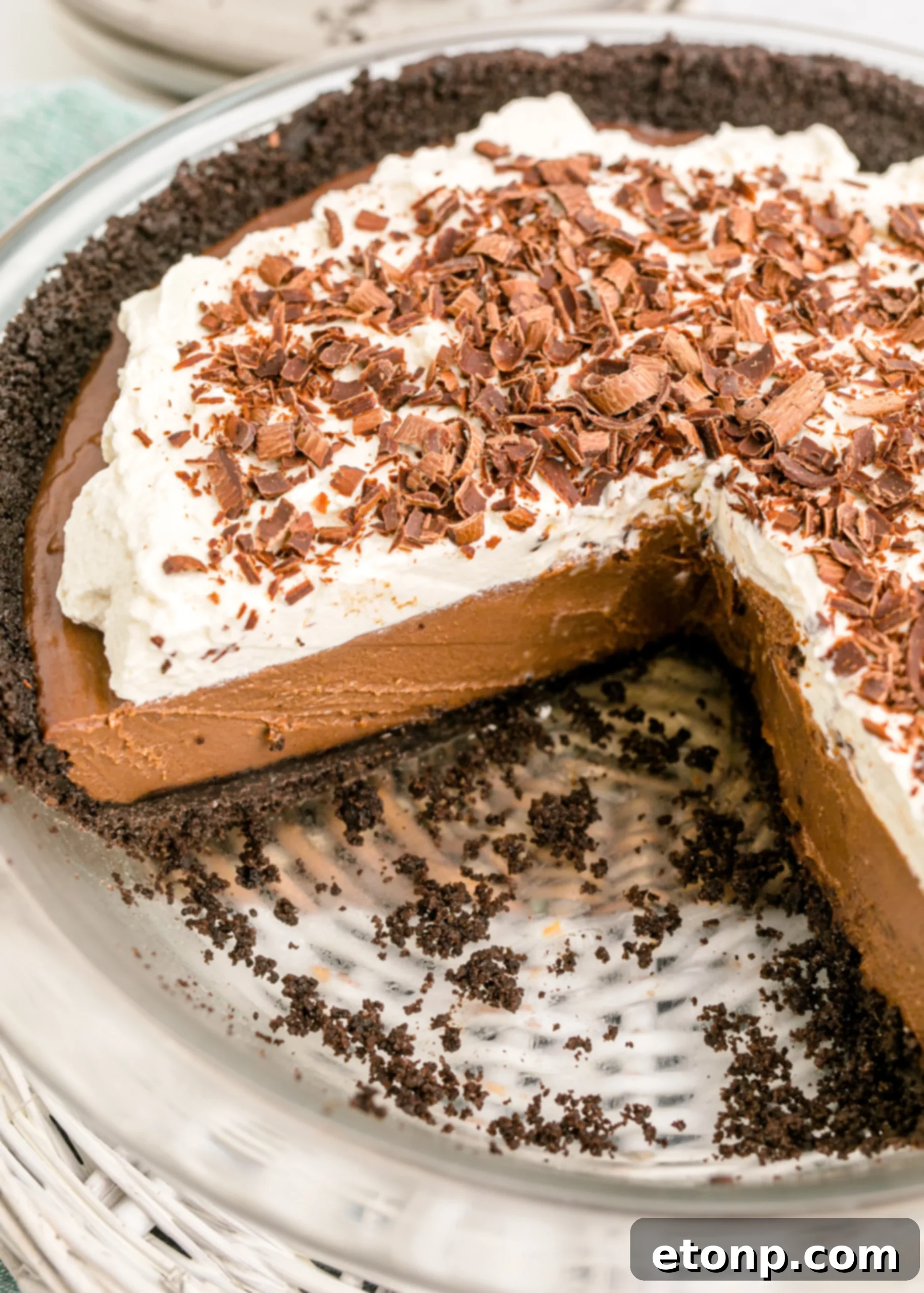 Chocolate Cream Pie topped with whipped cream and chocolate shavings in a white pie dish with a slice taken out, showcasing the layers