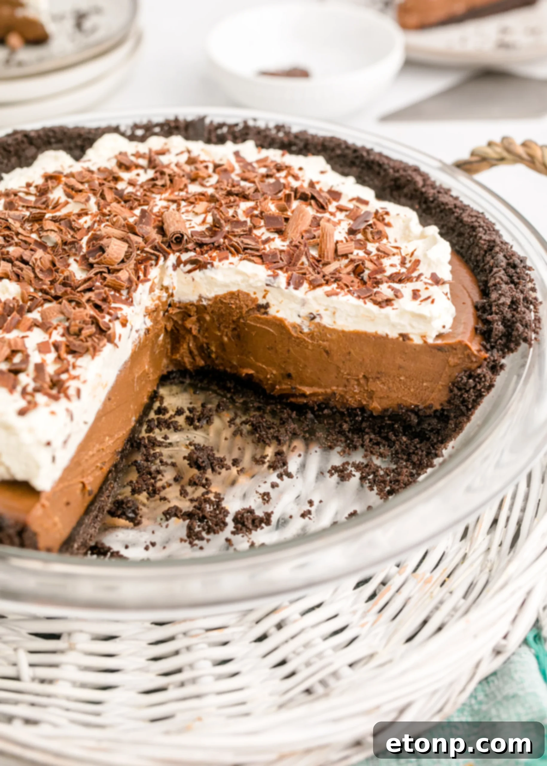 Chocolate Cream Pie topped with whipped cream and chocolate shavings in a white pie dish with a slice taken out, highlighting its deliciousness