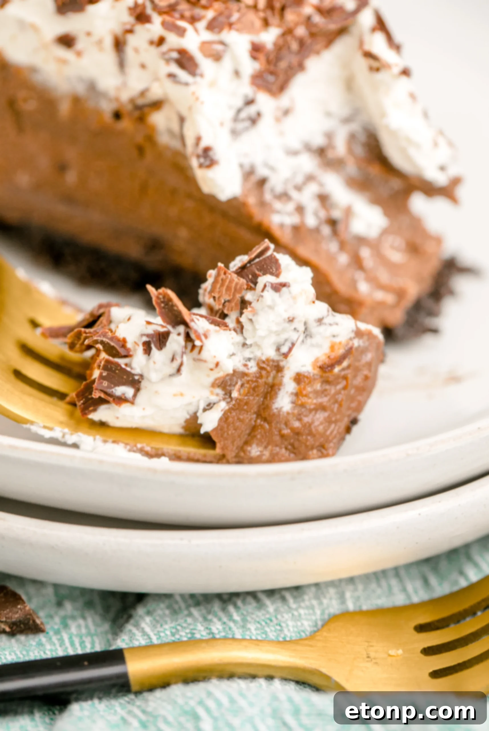 Chocolate Cream Pie topped with whipped cream and chocolate shavings on a white plate with a gold fork, showing a perfect bite