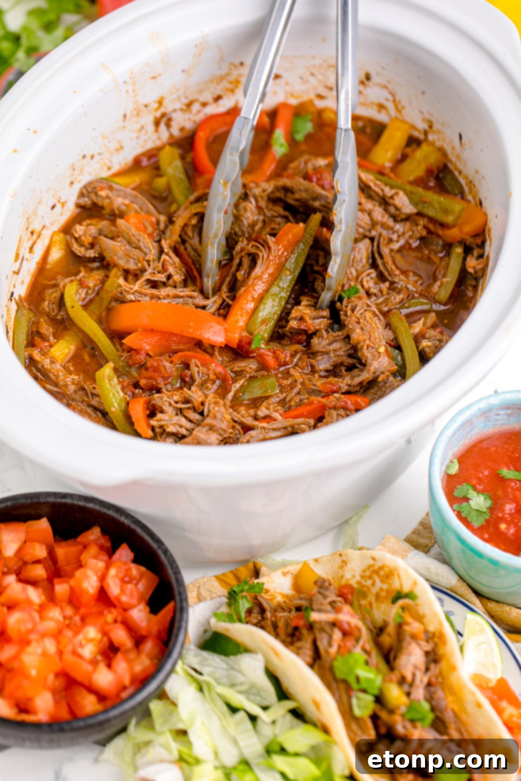 Steak Fajitas in a crock pot with tongs lifting the steak, with a bowl of salasa next to it
