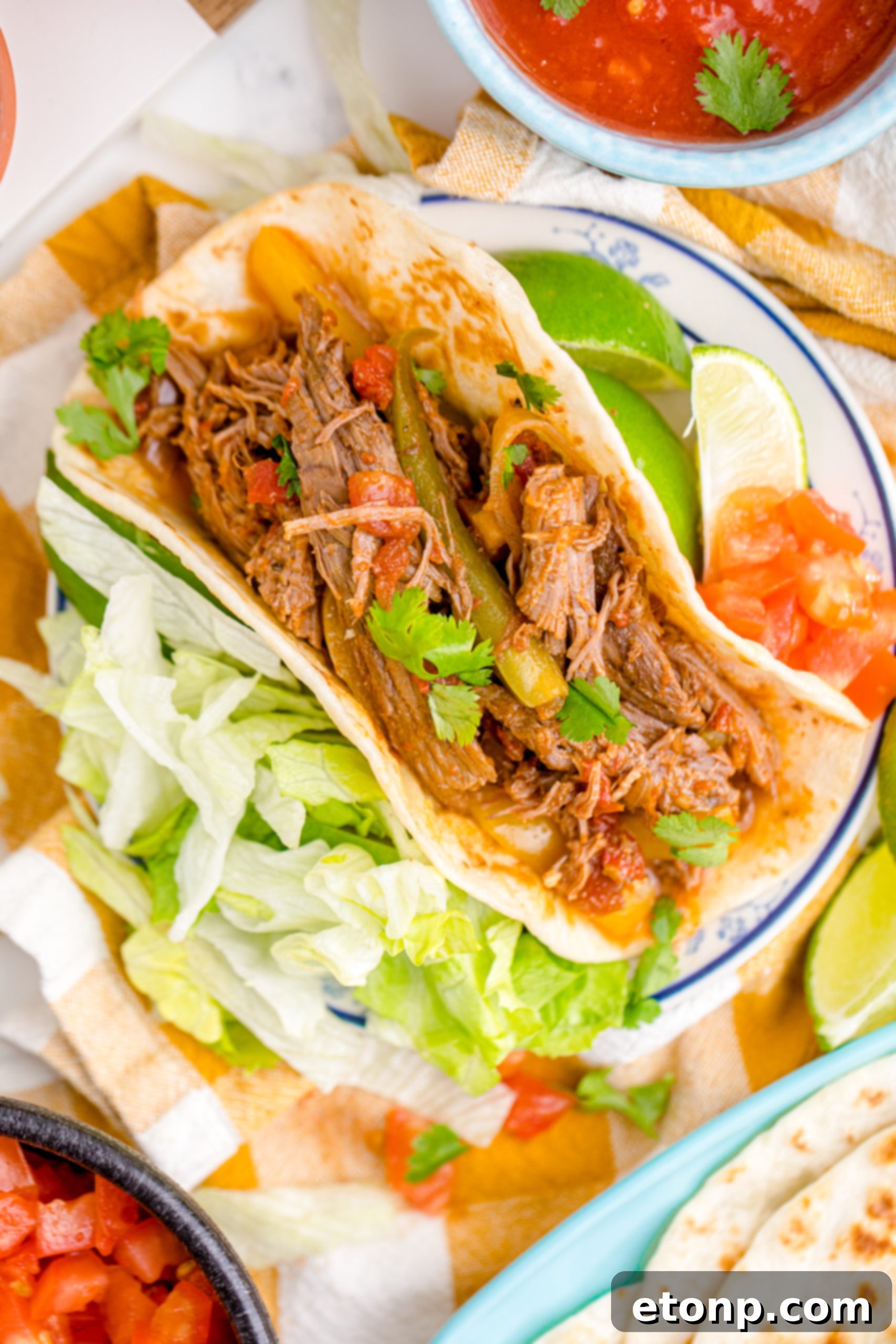 Steak Fajitas wrapped in a tortilla with lettuce piled next to it and limes with salsa