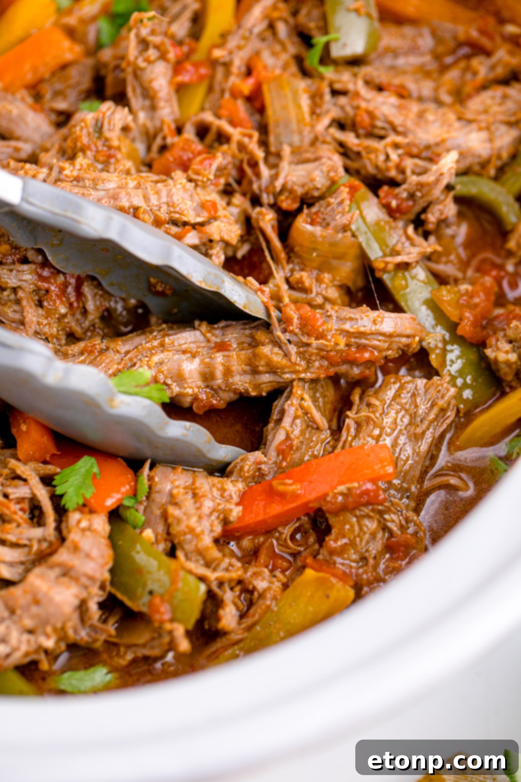 Steak Fajitas in a white crock pot being lifted with tongs