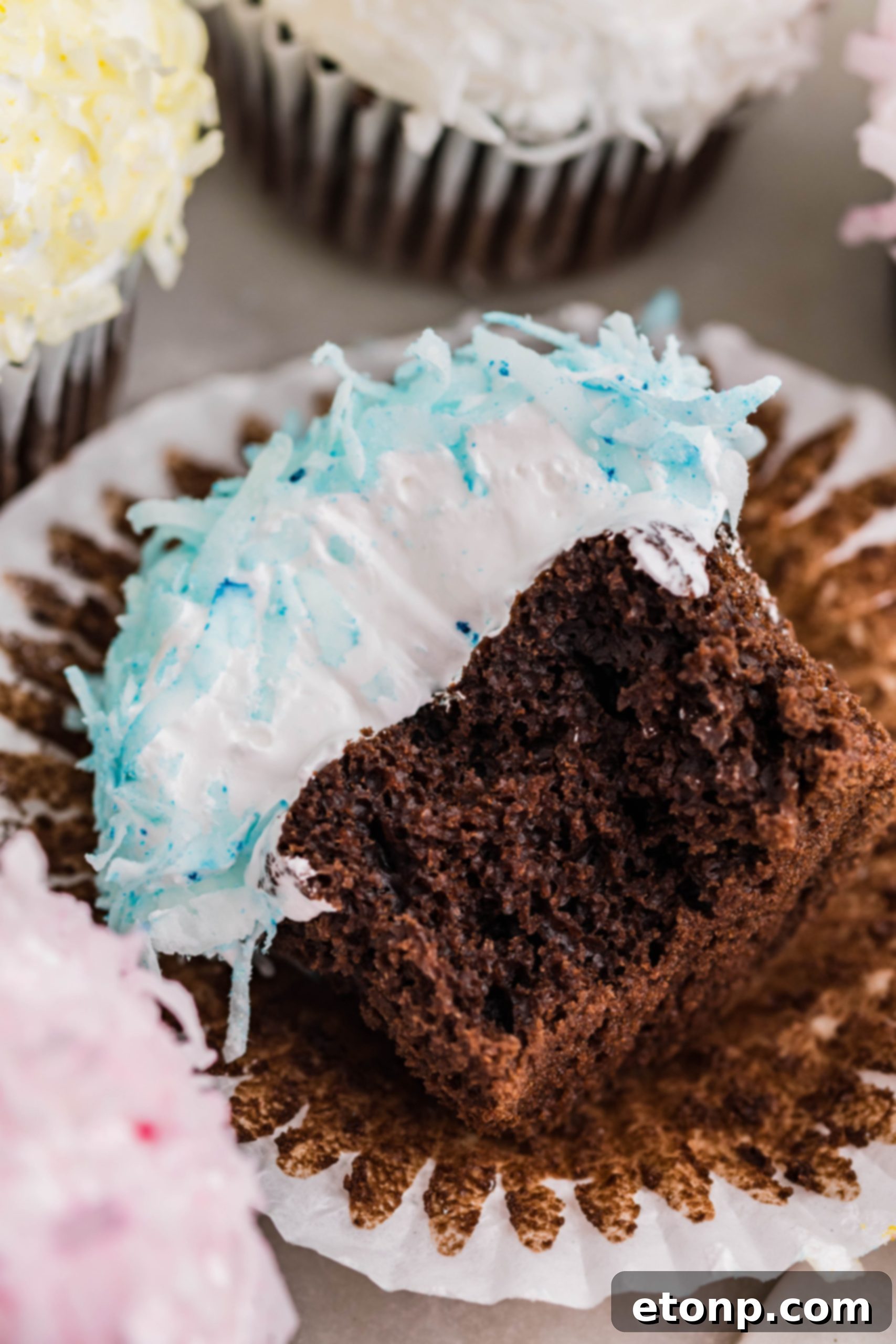 A tantalizing view of a chocolate cupcake, adorned with blue coconut shavings and fluffy marshmallow frosting, resting on its side after a delicious bite has been taken.