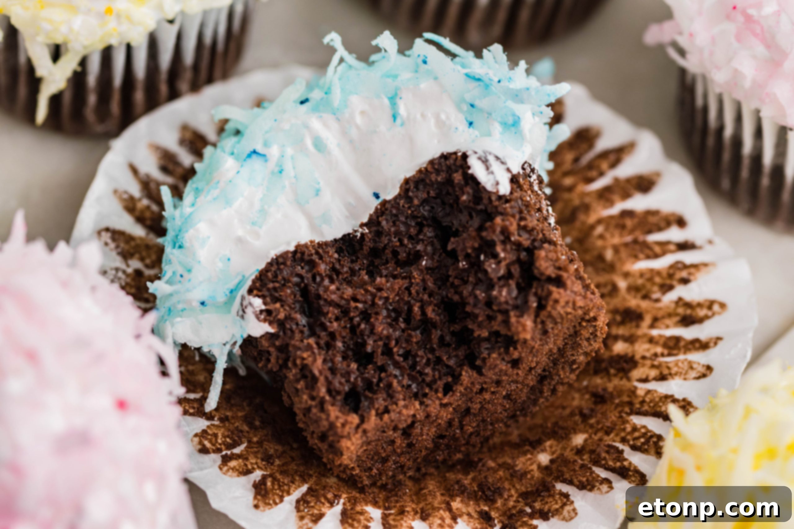 A beautifully composed flat lay of a chocolate cupcake, featuring vibrant blue coconut shavings and marshmallow frosting, elegantly presented on its side after a delightful bite.