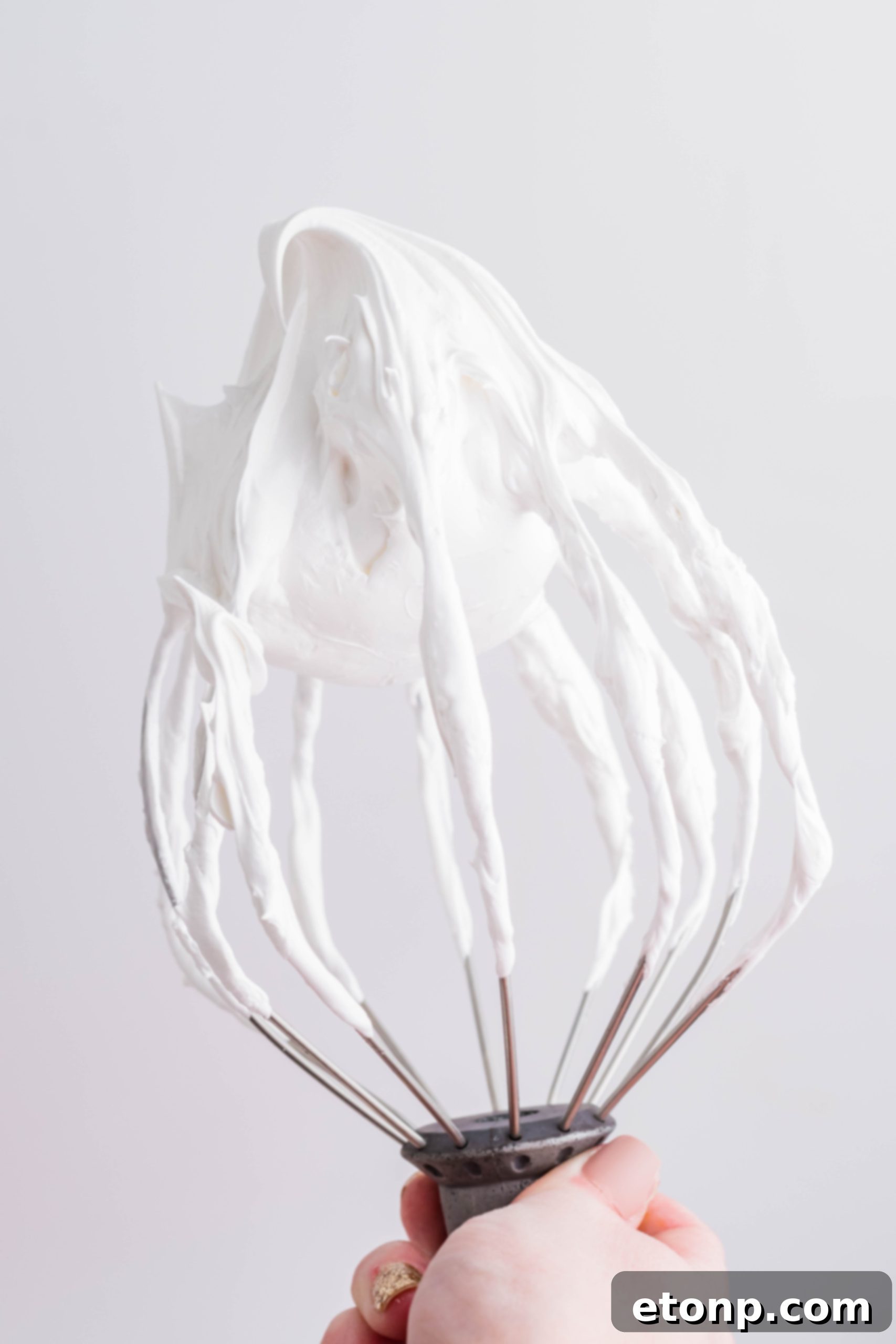 Fluffy, homemade marshmallow frosting clinging perfectly to the tines of a whisk, highlighting its light and airy consistency.