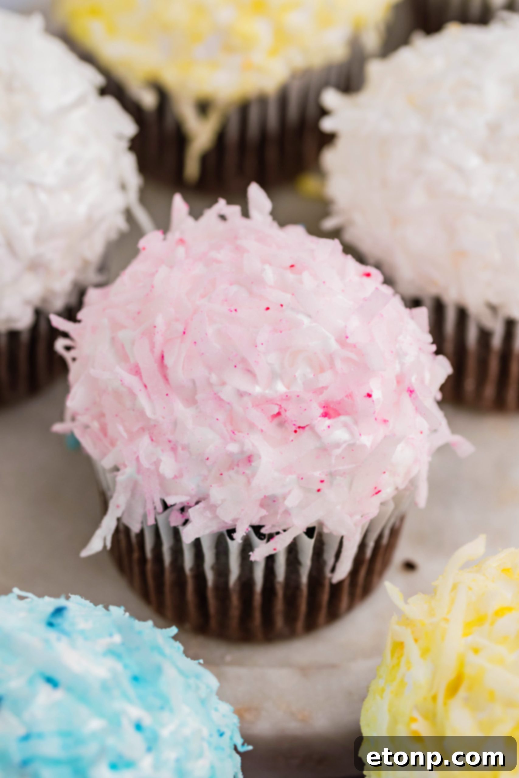 A beautifully presented chocolate cupcake, adorned with fluffy pink coconut shavings and a generous swirl of marshmallow frosting, resting delicately on a marble platter.