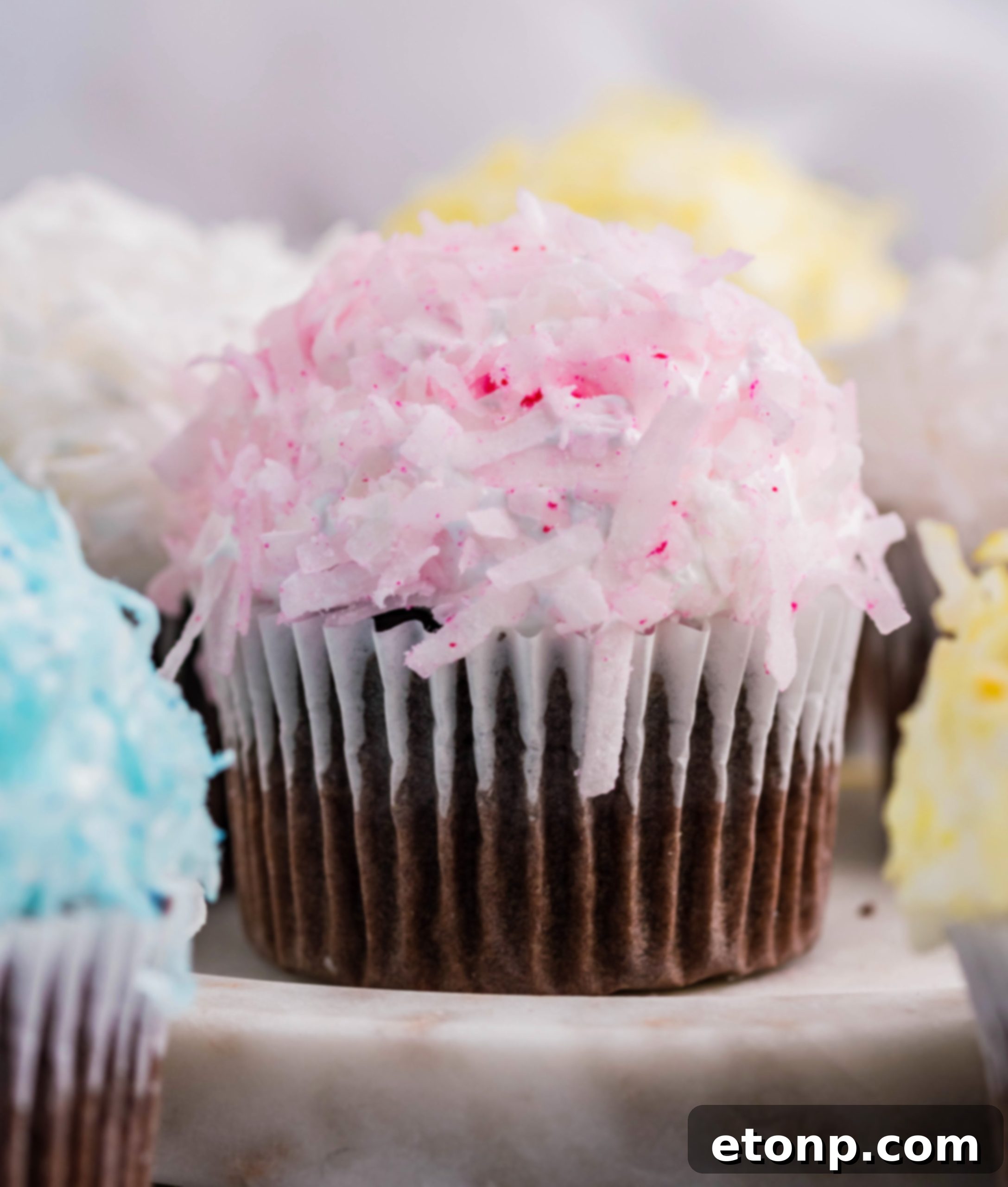 Another mouthwatering chocolate cupcake, adorned with delicate pink coconut shavings and a generous dollop of marshmallow frosting, artfully placed on a pristine marble platter.