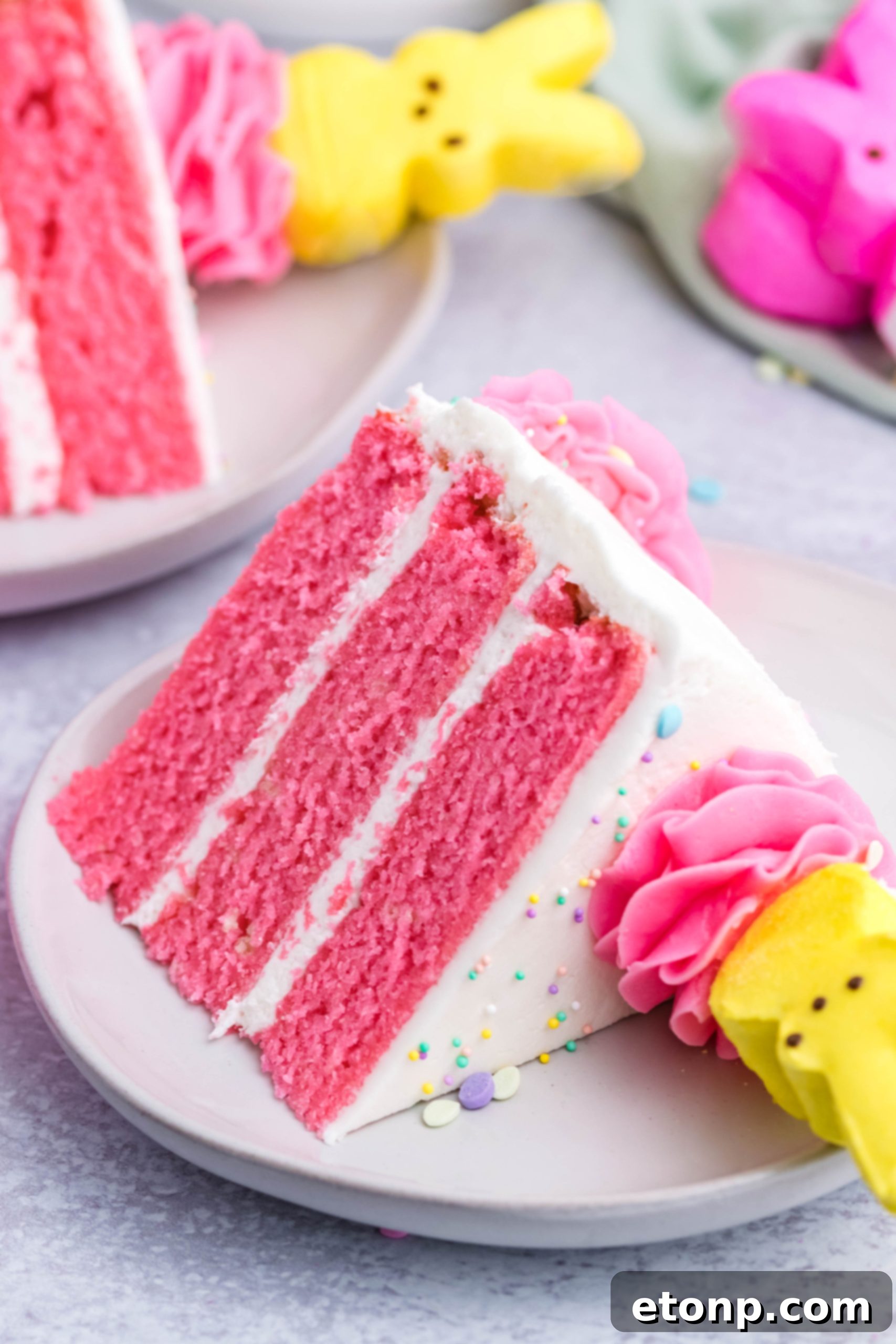 Pink Vanilla layered cake with white frosting and yellow Peeps for Easter on a white plate with two other slices next to it
