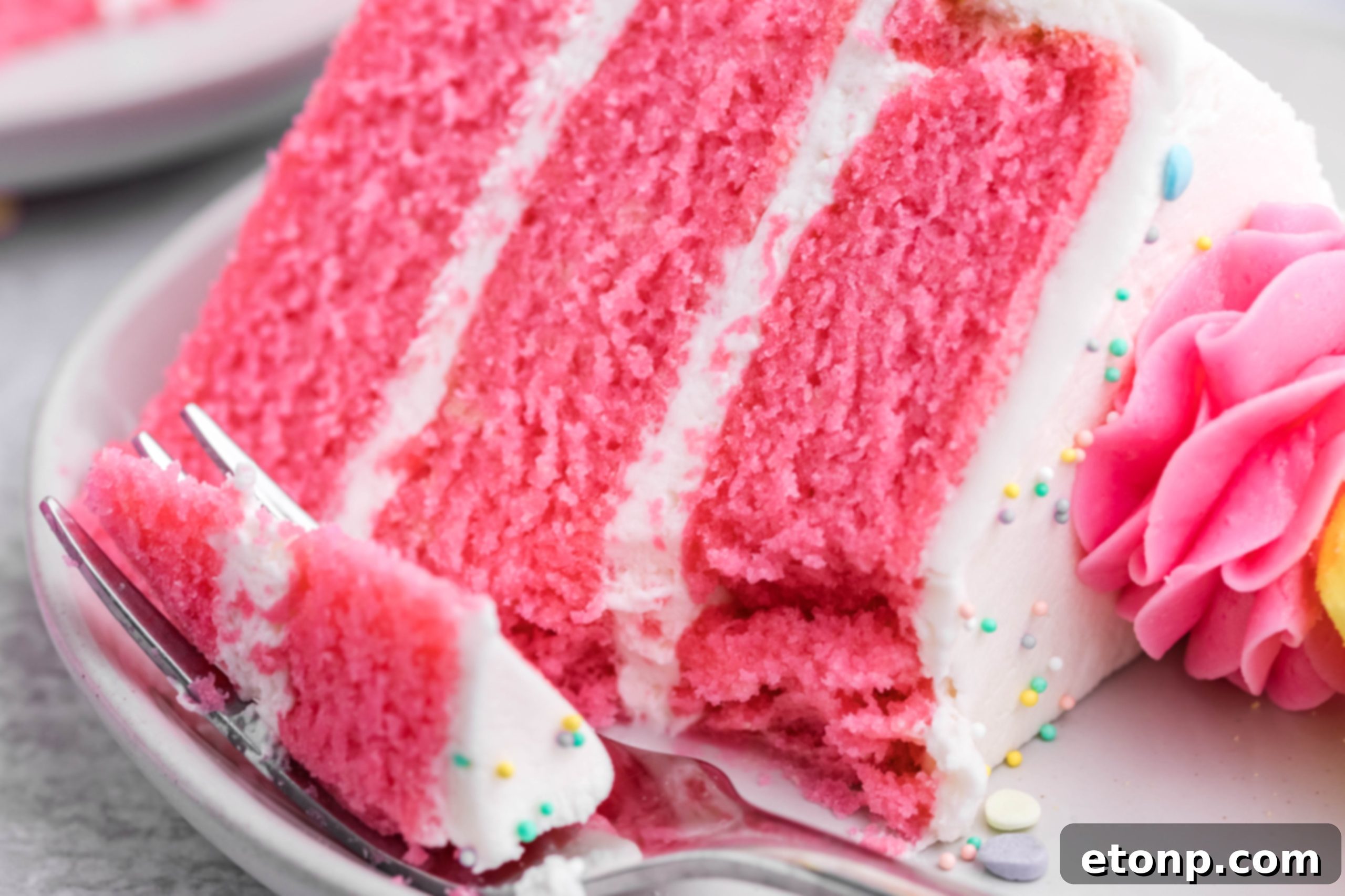 Pink Vanilla layered cake with white frosting and topped with yellow Peeps for Easter on a white plate with a slice gone and a bite on a fork ready to be eaten