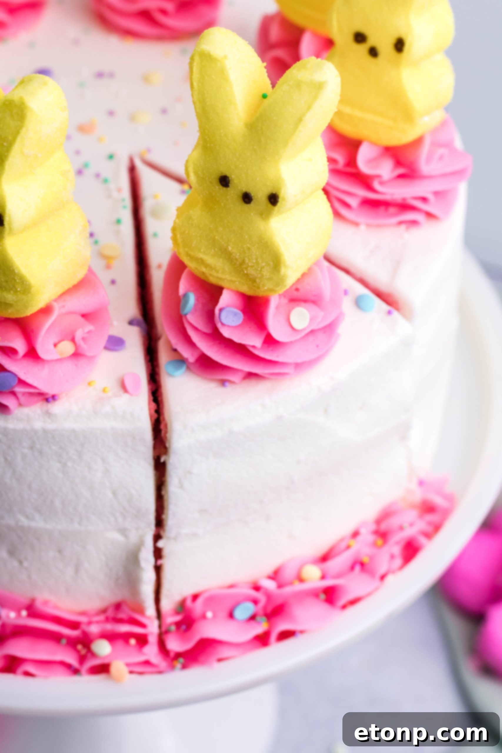 Overhead shot of a pink Vanilla layered cake with white frosting and topped with yellow Peeps for Easter on a white cake stand