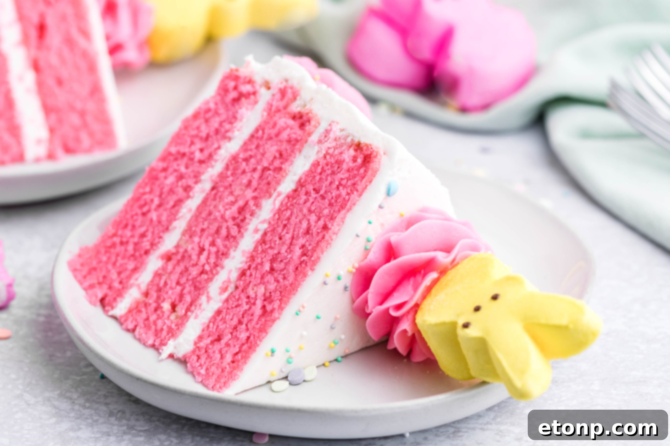 A slice of pink Vanilla layered cake with white frosting and yellow Peeps for Easter on a white plate