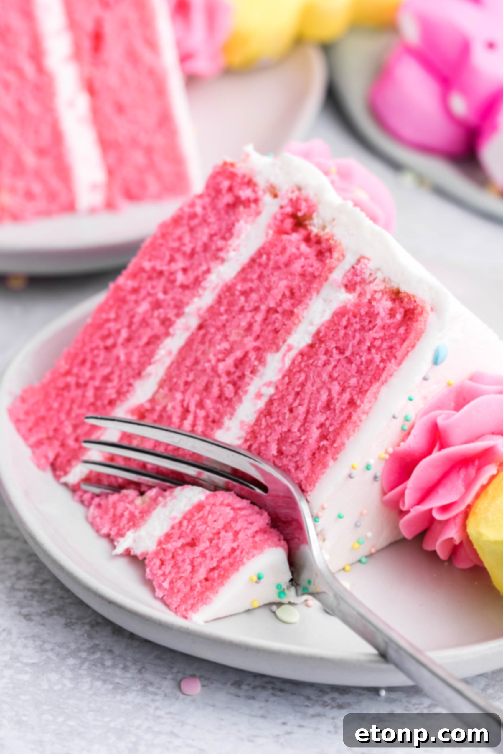 A fork slicing into a pink Vanilla layered cake with white frosting and yellow Peeps for Easter on a white plate