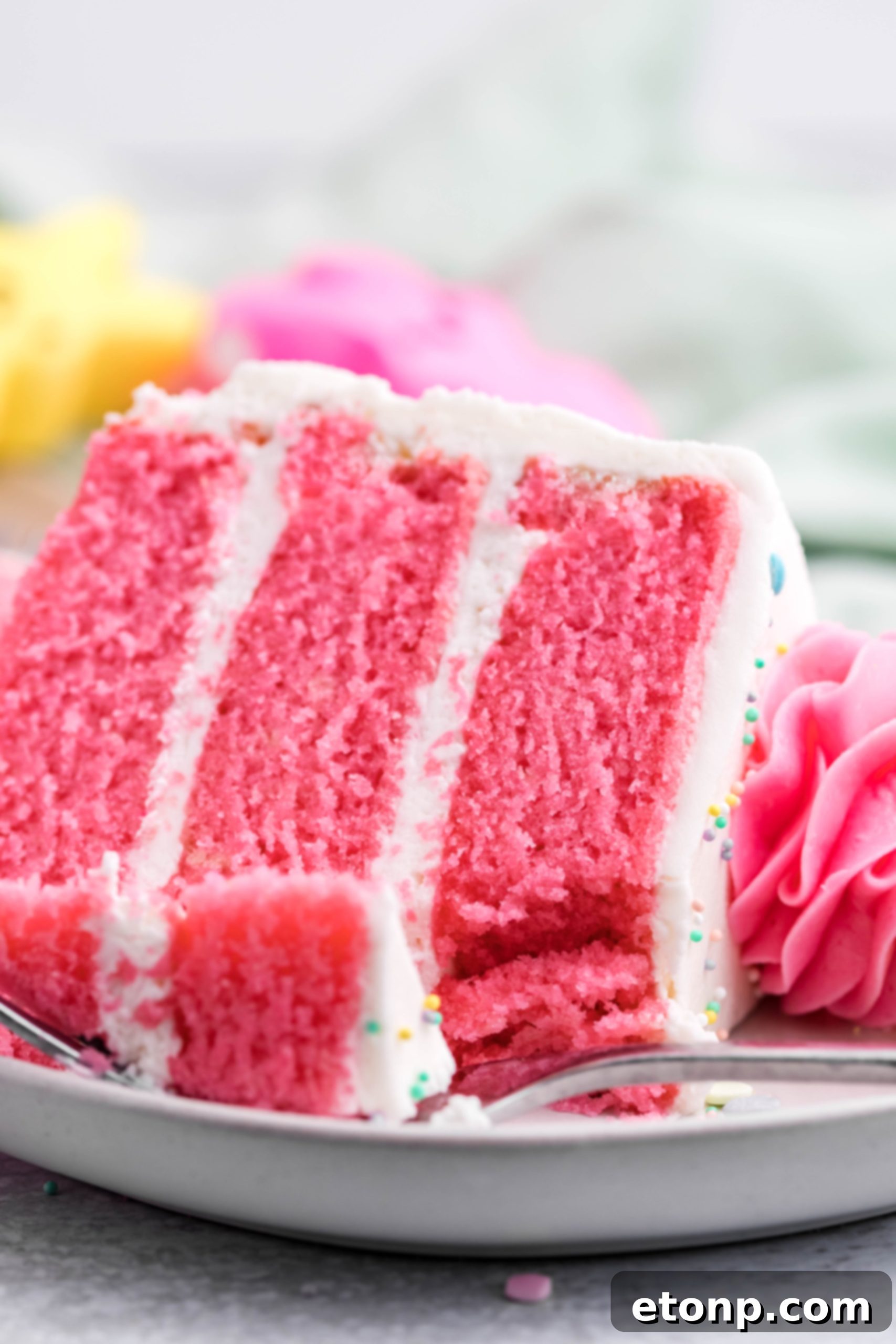 Pink Vanilla layered cake with white frosting and topped with yellow Peeps for Easter on a white plate with a slice gone