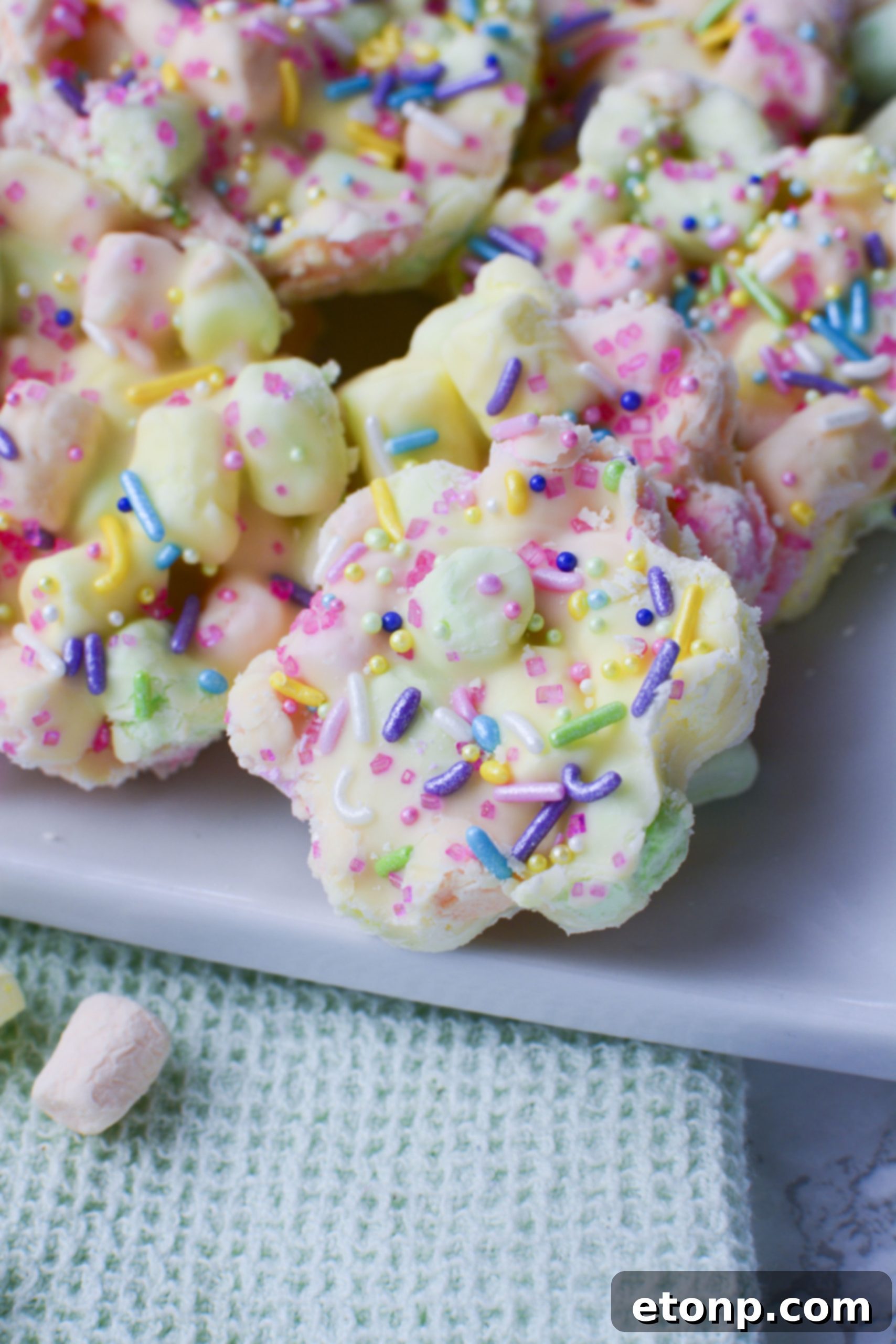 Easter Marshmallow treats with pink, green and yellow mini marshmallows cut into the shape of flowers on a square white plate