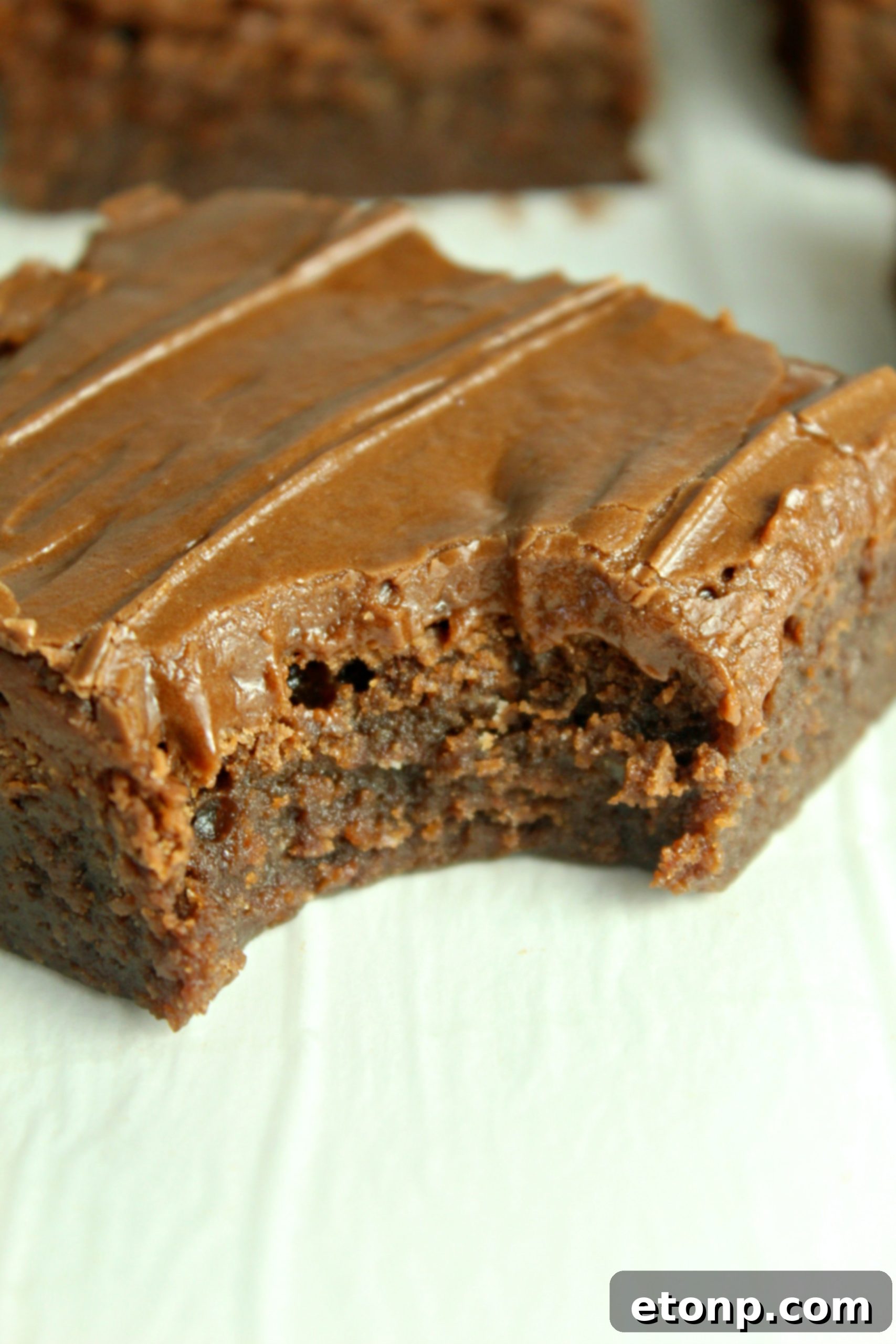 Homemade chocolate frosted lunch lady Brownies with a bite gone on a white table
