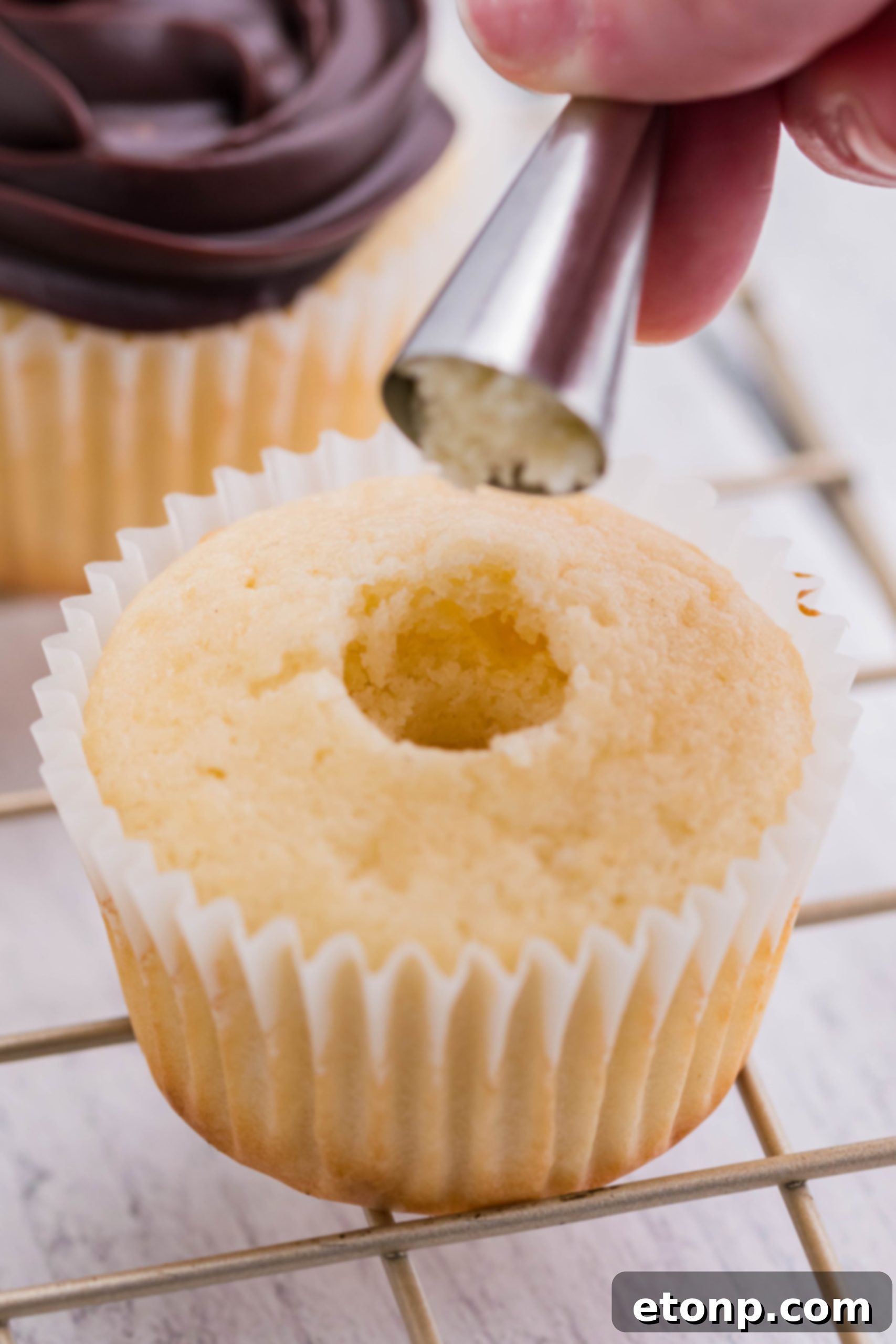 A baker carefully removes a cylindrical piece from the center of a Boston Cream Cupcake to create space for the luscious cream filling.