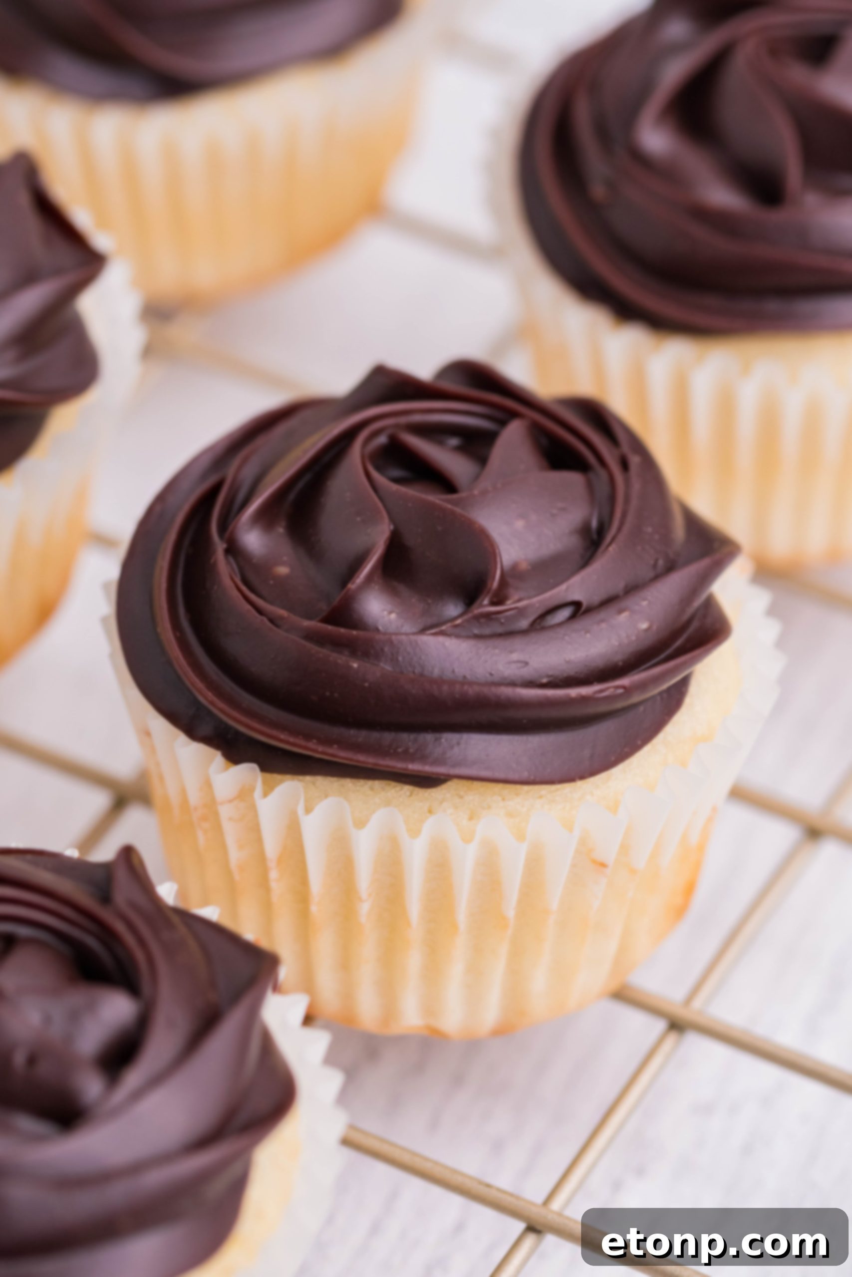 Another side perspective of irresistible Boston Cream Cupcakes, artfully arranged on a cooling rack, showcasing their exquisite toppings.