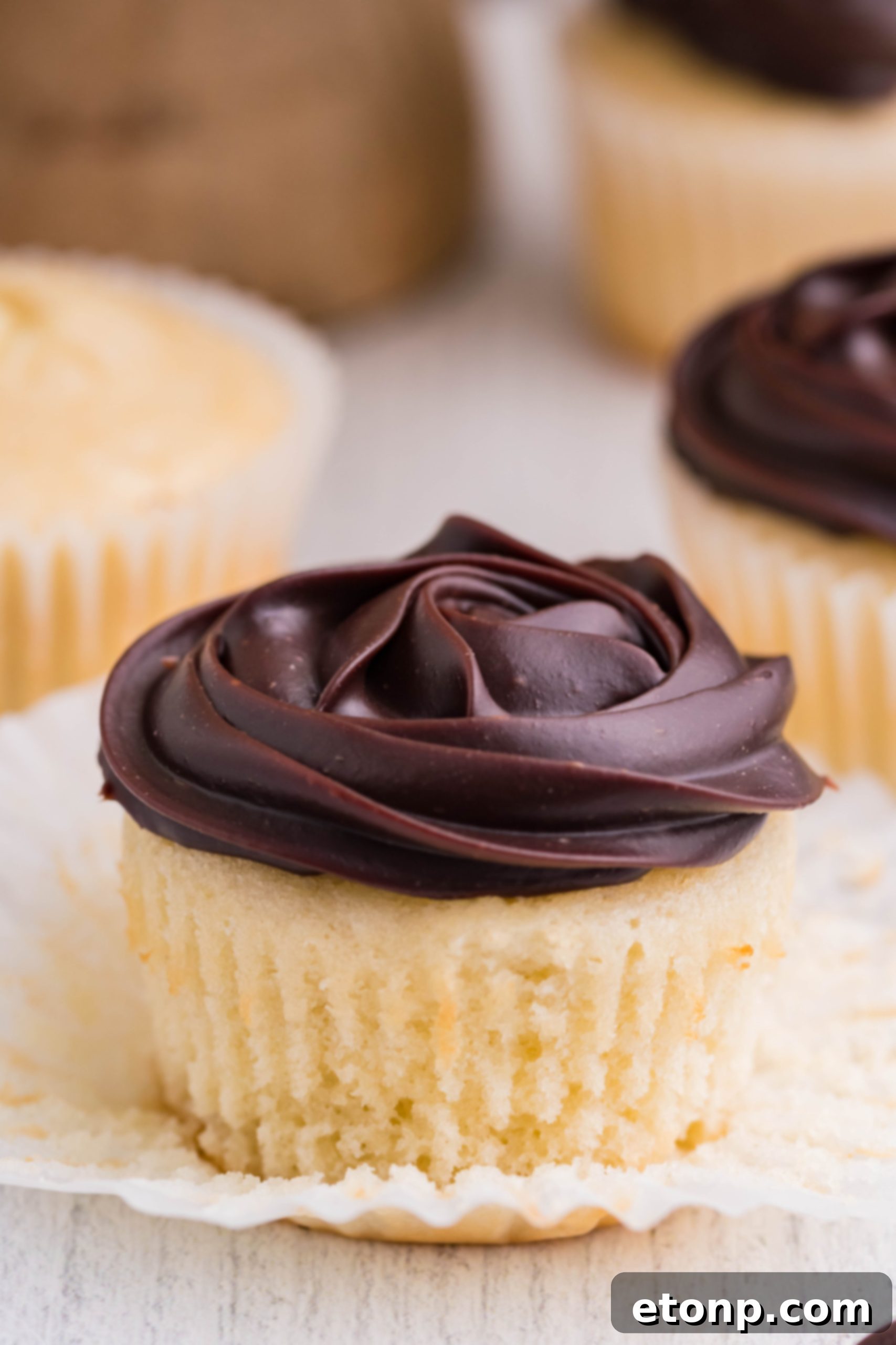 A close-up side shot of Boston Cream Cupcakes on a white kitchen counter, highlighting their perfect chocolate glaze and cream filling.