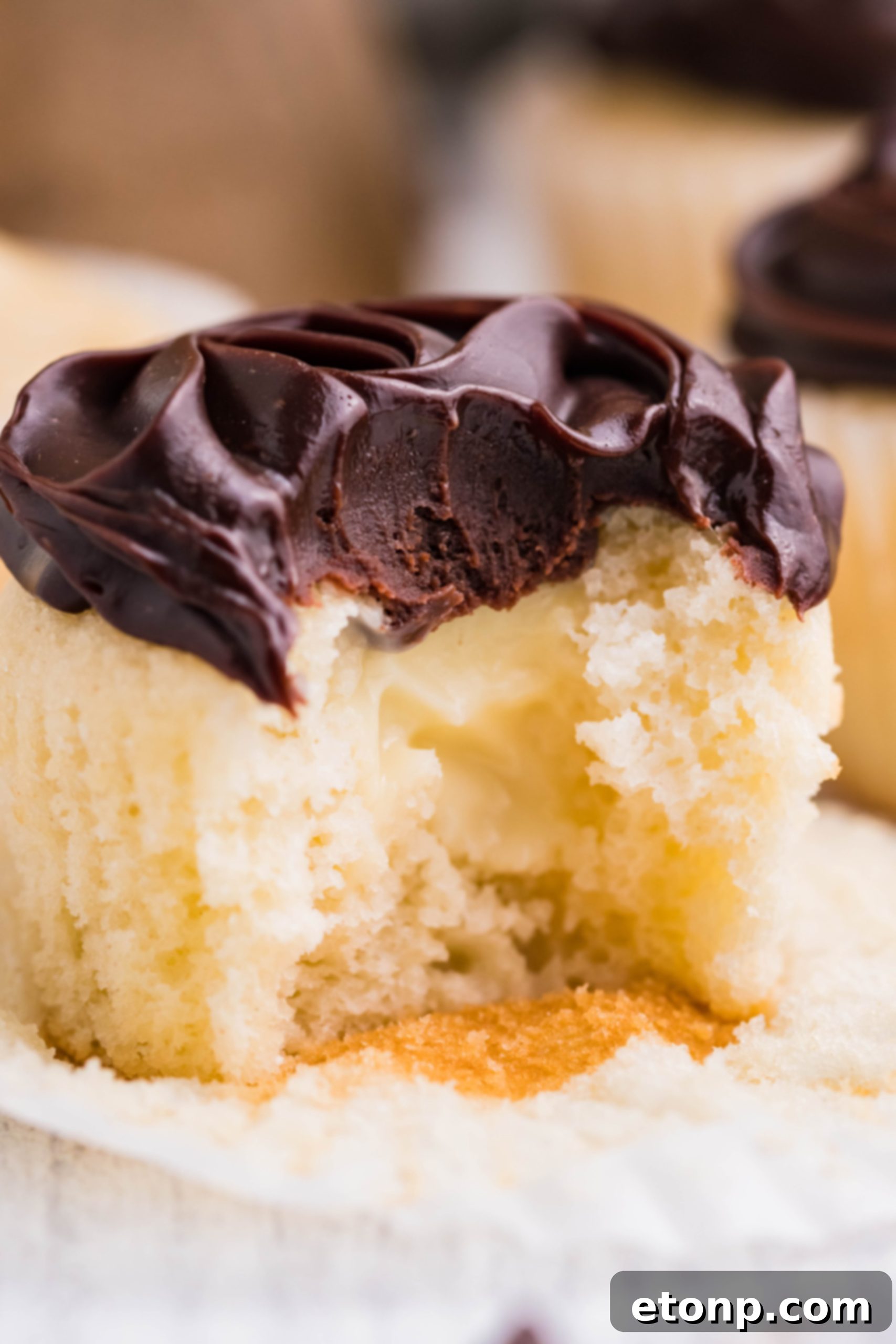 A delicious Boston Cream Cupcake on a white counter with a section removed, revealing its creamy vanilla filling and inviting texture.