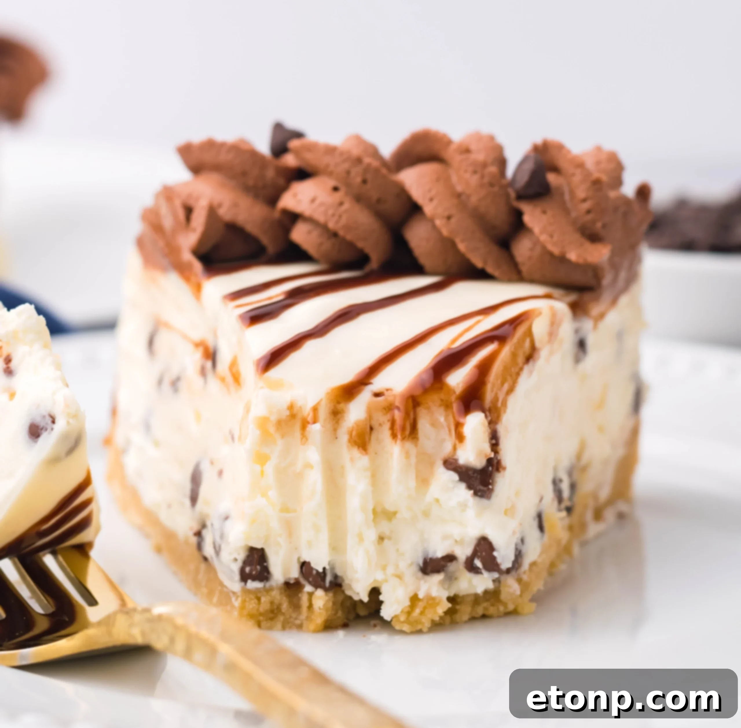 A slice of Chocolate Chip Cheesecake on a white plate with a bite taken out, accompanied by a gold fork.