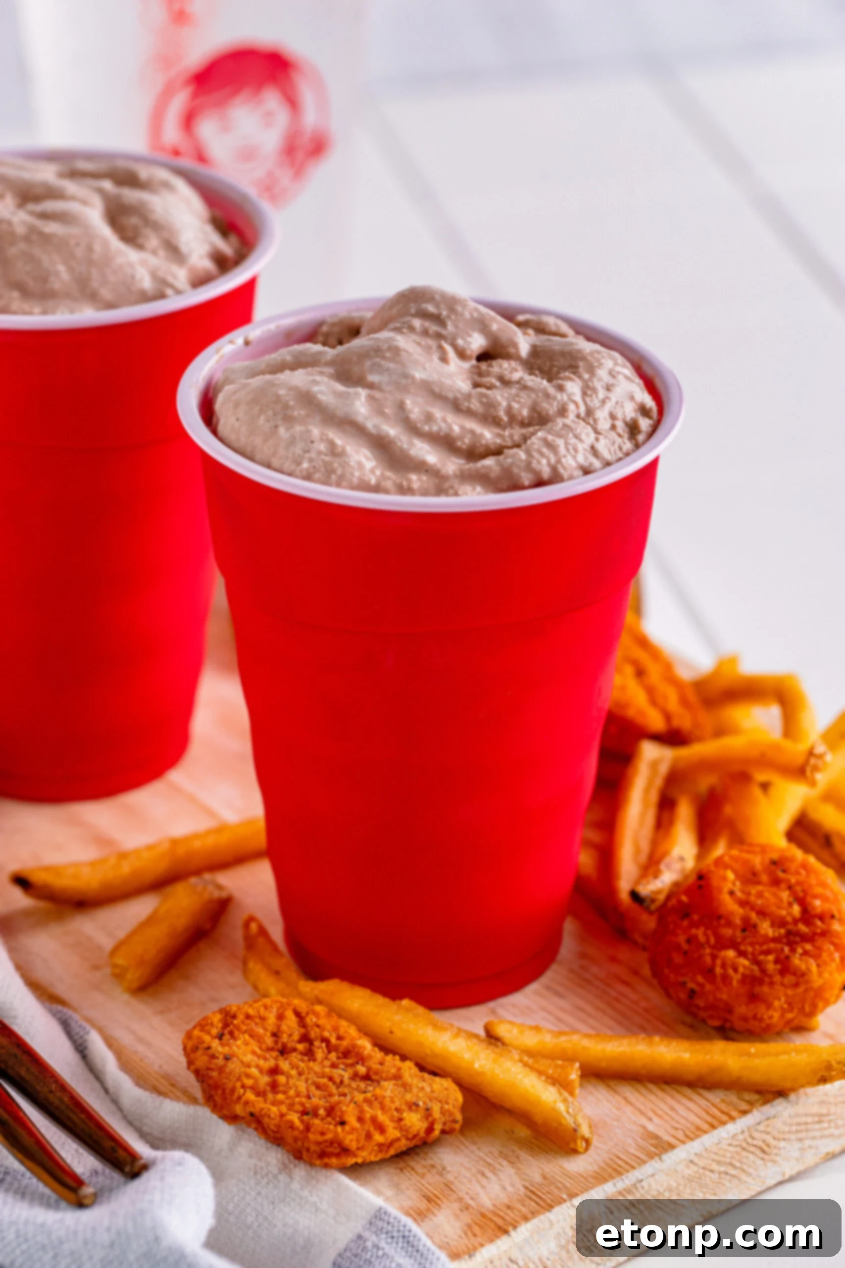 Homemade Wendy's Frosty in a red solo cup, surrounded by crispy chicken nuggets and golden fries, creating a complete fast-food experience at home.