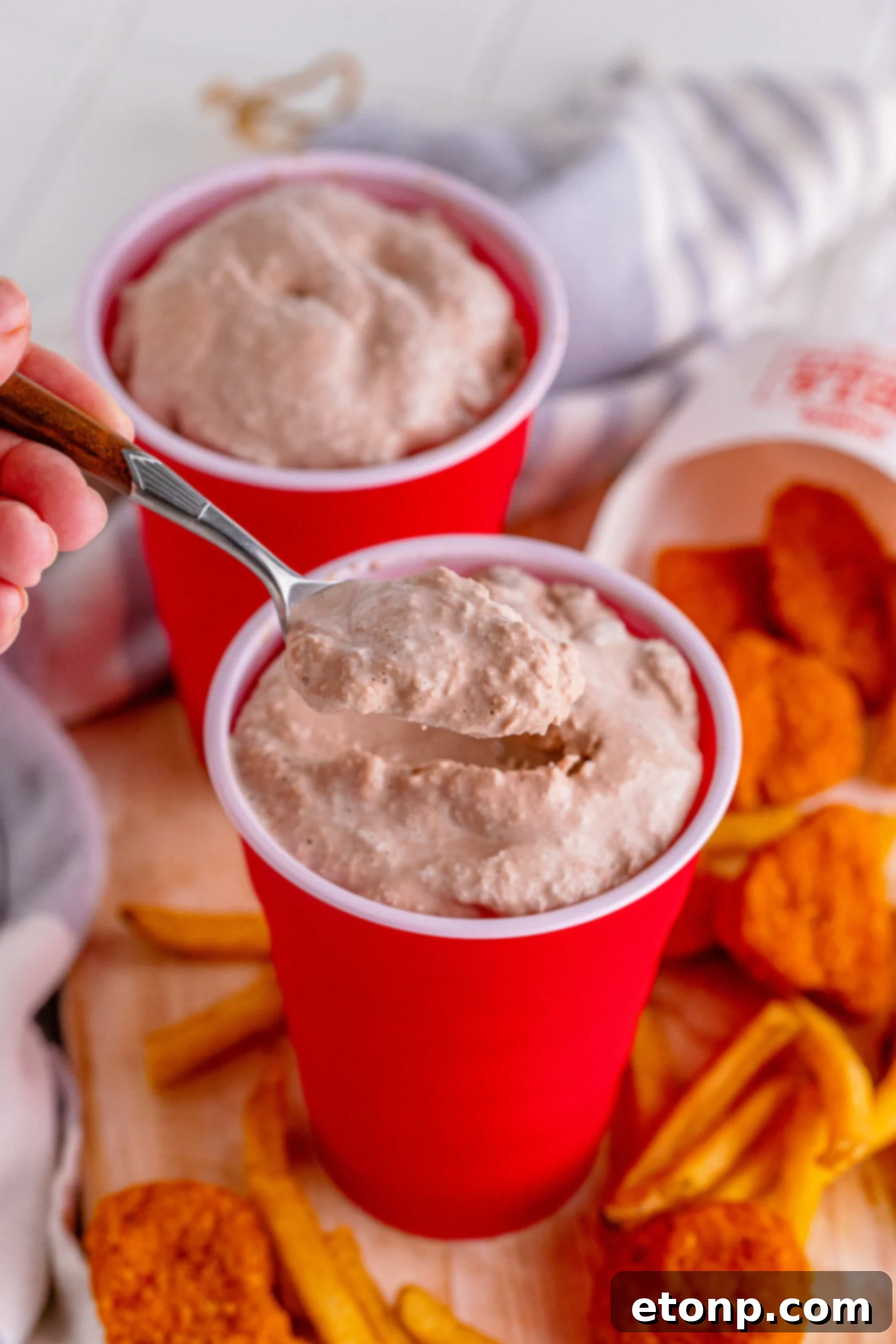 A homemade Wendy's Frosty in a red solo cup, with a spoon scooping out a generous portion, emphasizing its creamy texture.