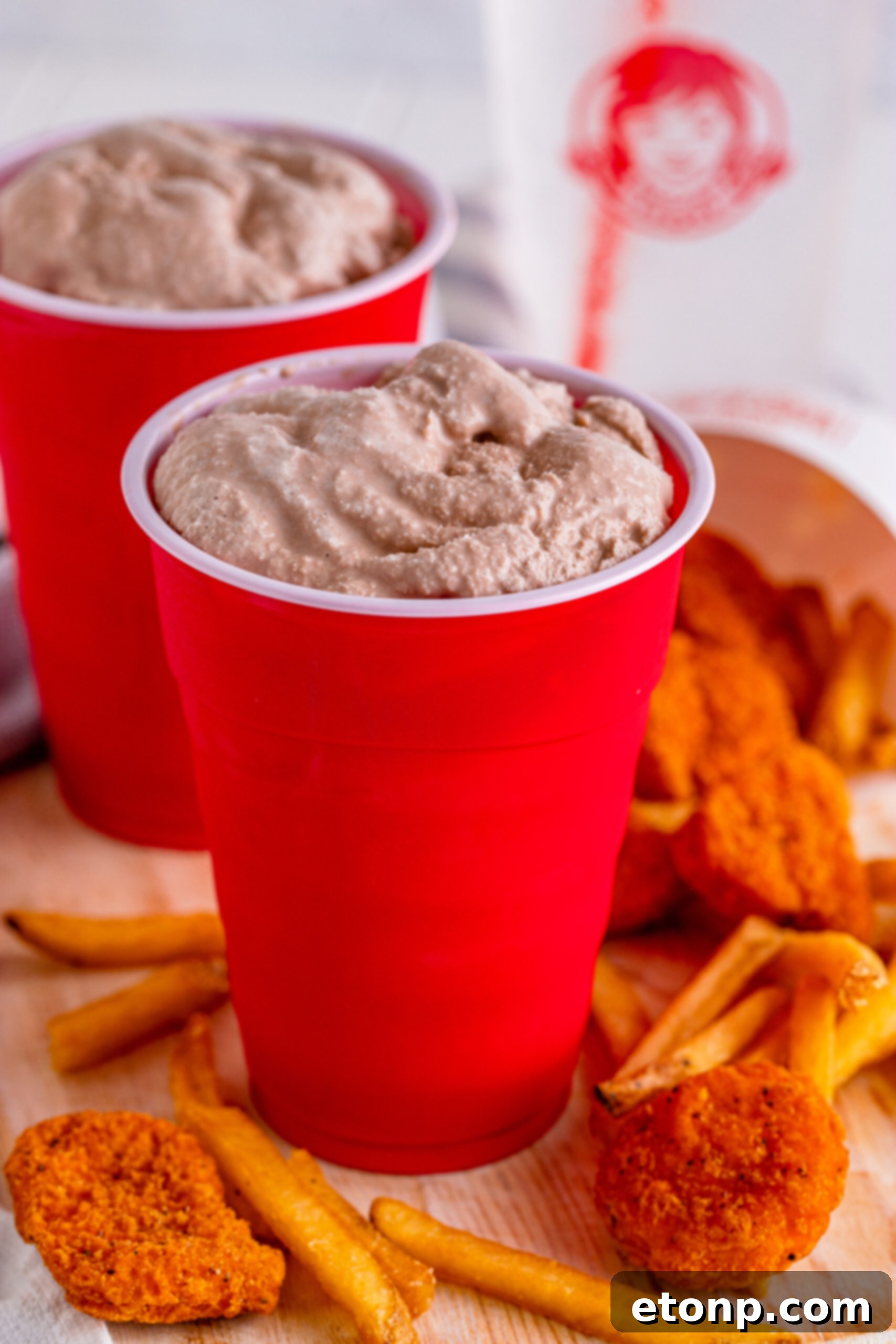 Homemade Wendy's Frosty in a red solo cup, surrounded by crispy fries and chicken nuggets, mimicking the classic Wendy's meal.
