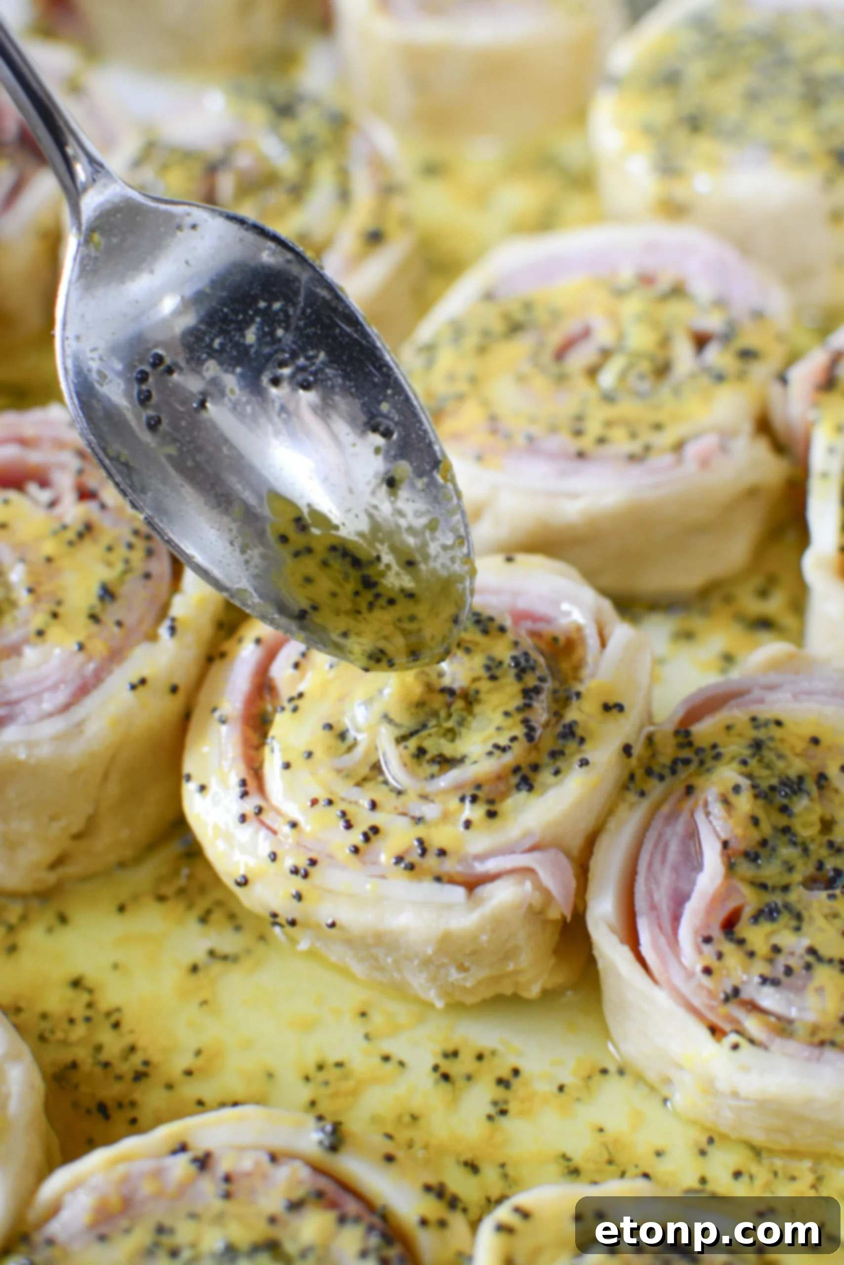 Ham and Cheese Pinwheels uncooked with dijon sauce being poured on top