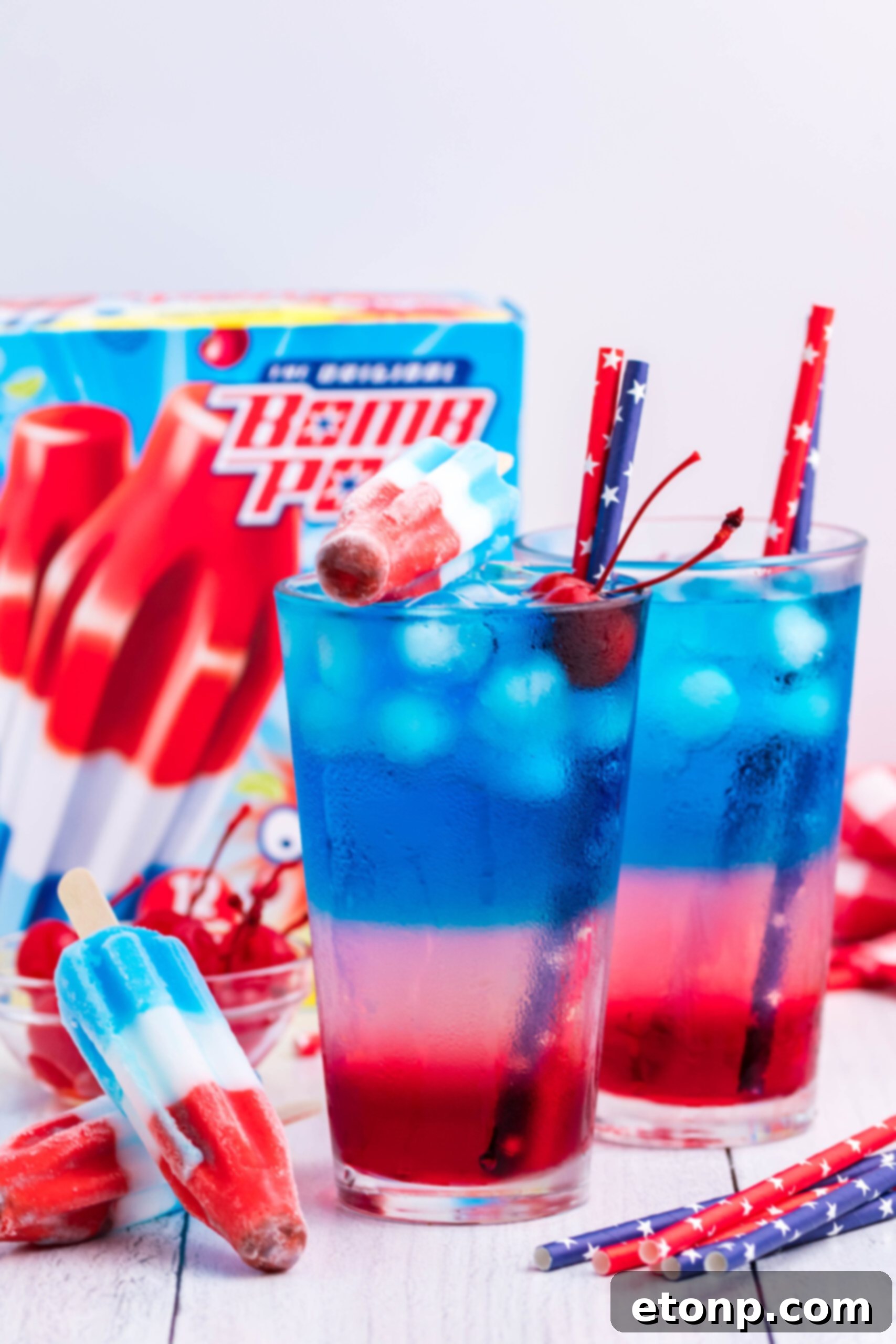 Bomb Pop Cocktail Drink in a clear glass with a blue & red straw with cherries floating far away shot