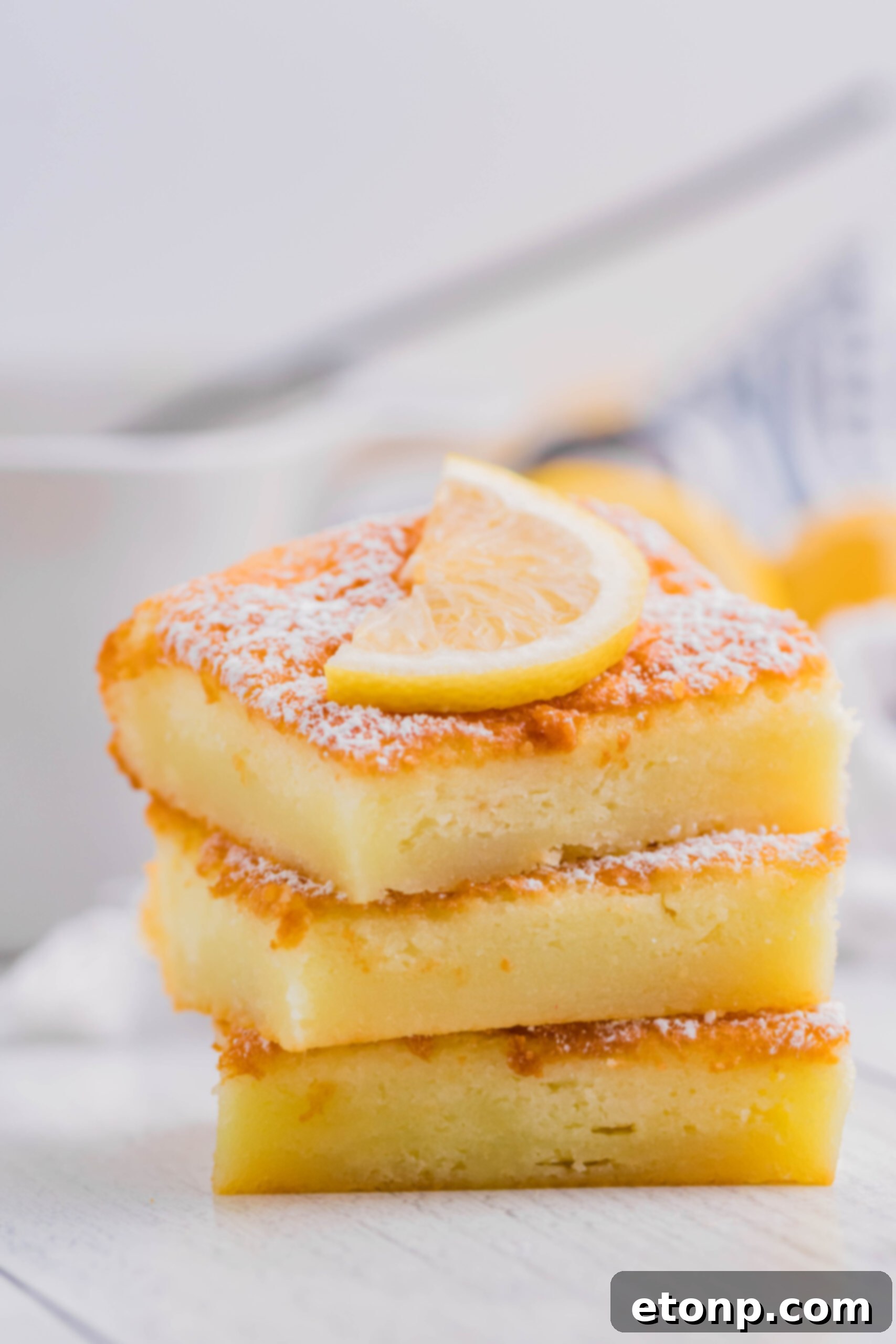 Several slices of 2-Ingredient Lemon Bars stacked neatly on a white plate, ready for serving
