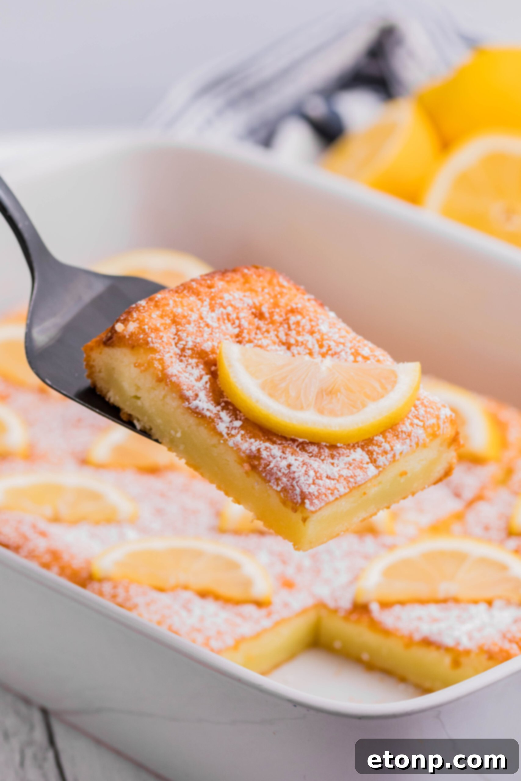 A delectable slice of 2-Ingredient Lemon Bar being lifted by a spatula, powdered sugar visible on top