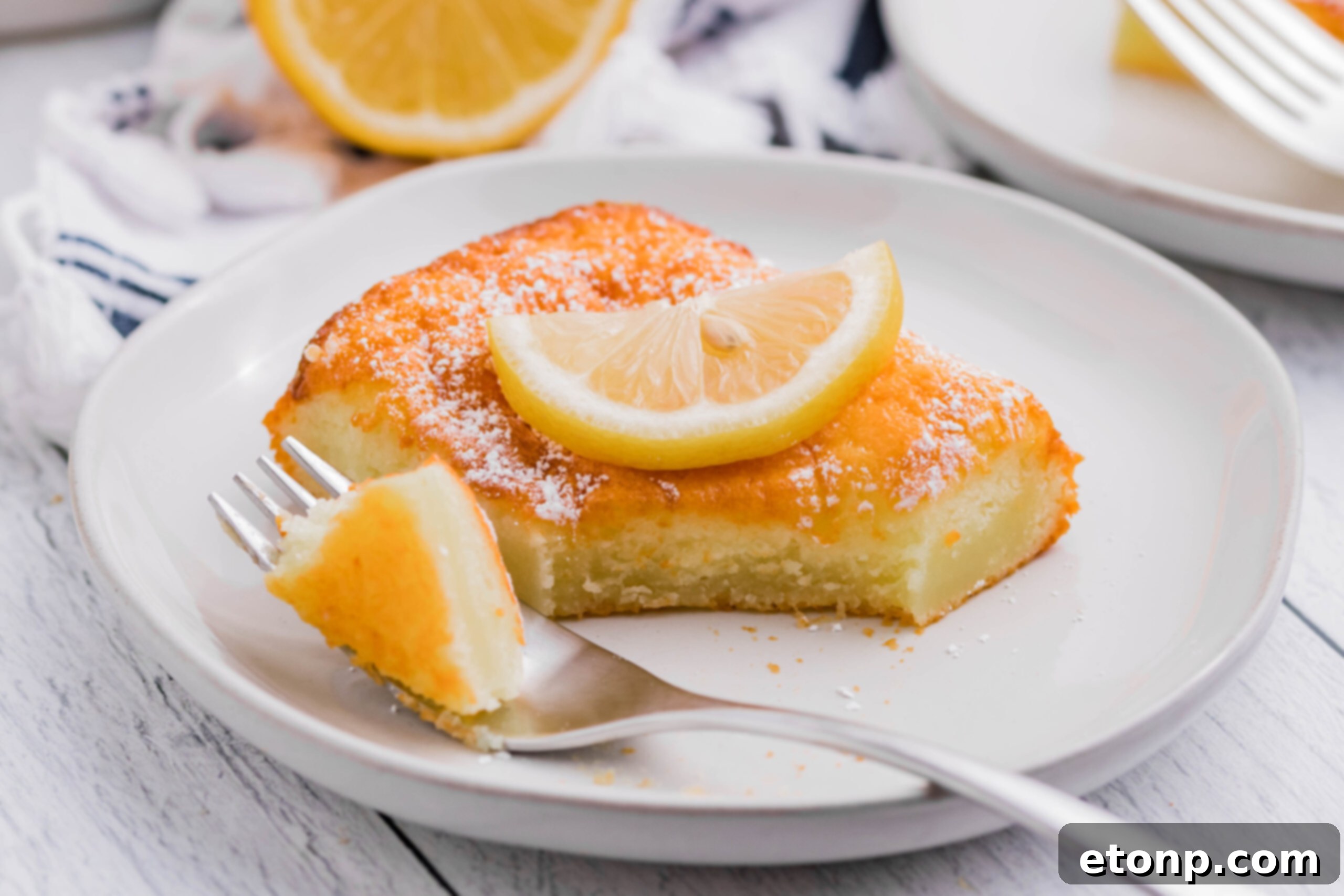 A 2-Ingredient Lemon Bar on a white plate with a fork taking a bite out, showing its fluffy texture