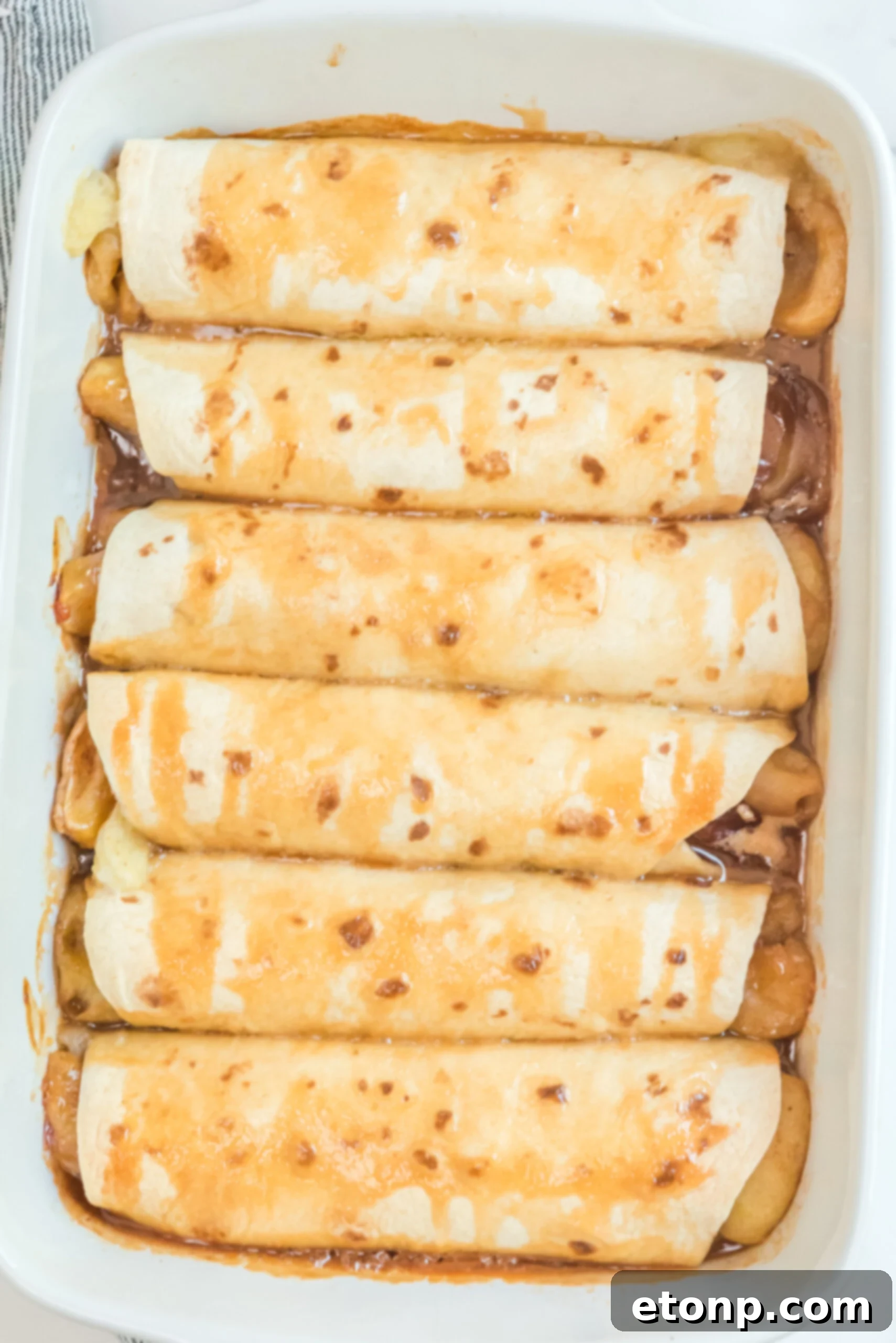 Cinnamon Apple Enchilada Bake 7 Overhead shot of Apple Pie Enchiladas generously topped with caramel sauce in a white baking dish