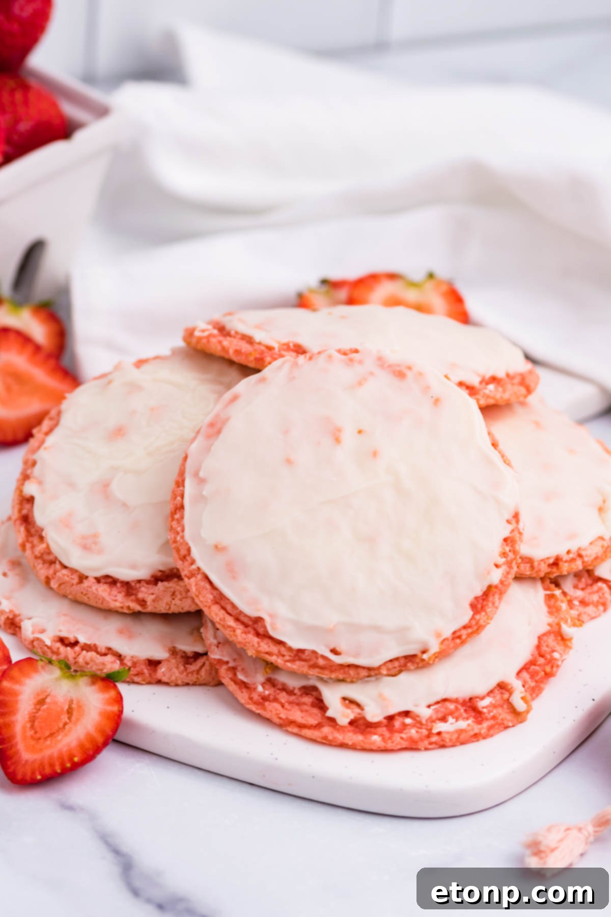Strawberry Cool Whip Cookies piled high on a white plate and surrounded by fresh sliced strawberries