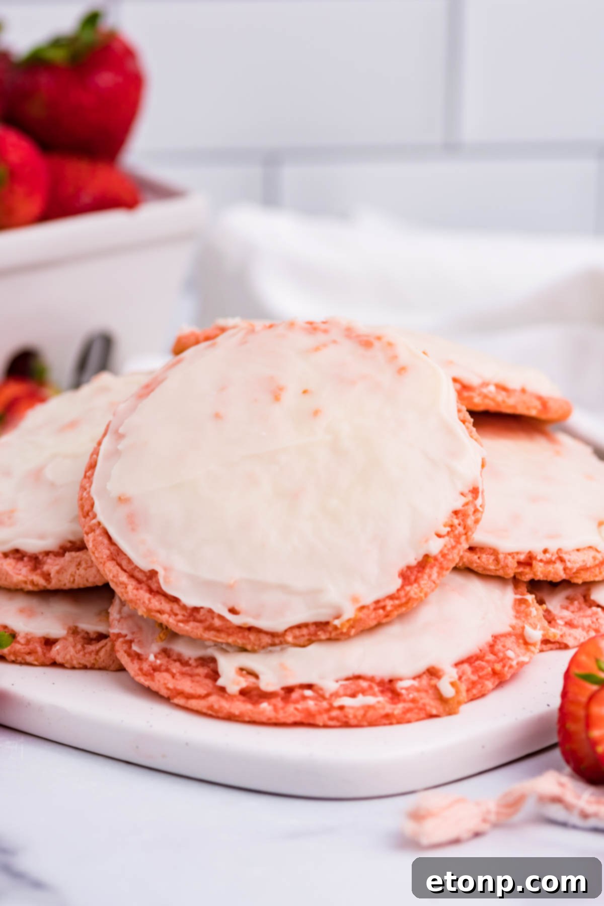 Strawberry Cool Whip Cookies with a container of fresh strawberries in the background, all on a white plate