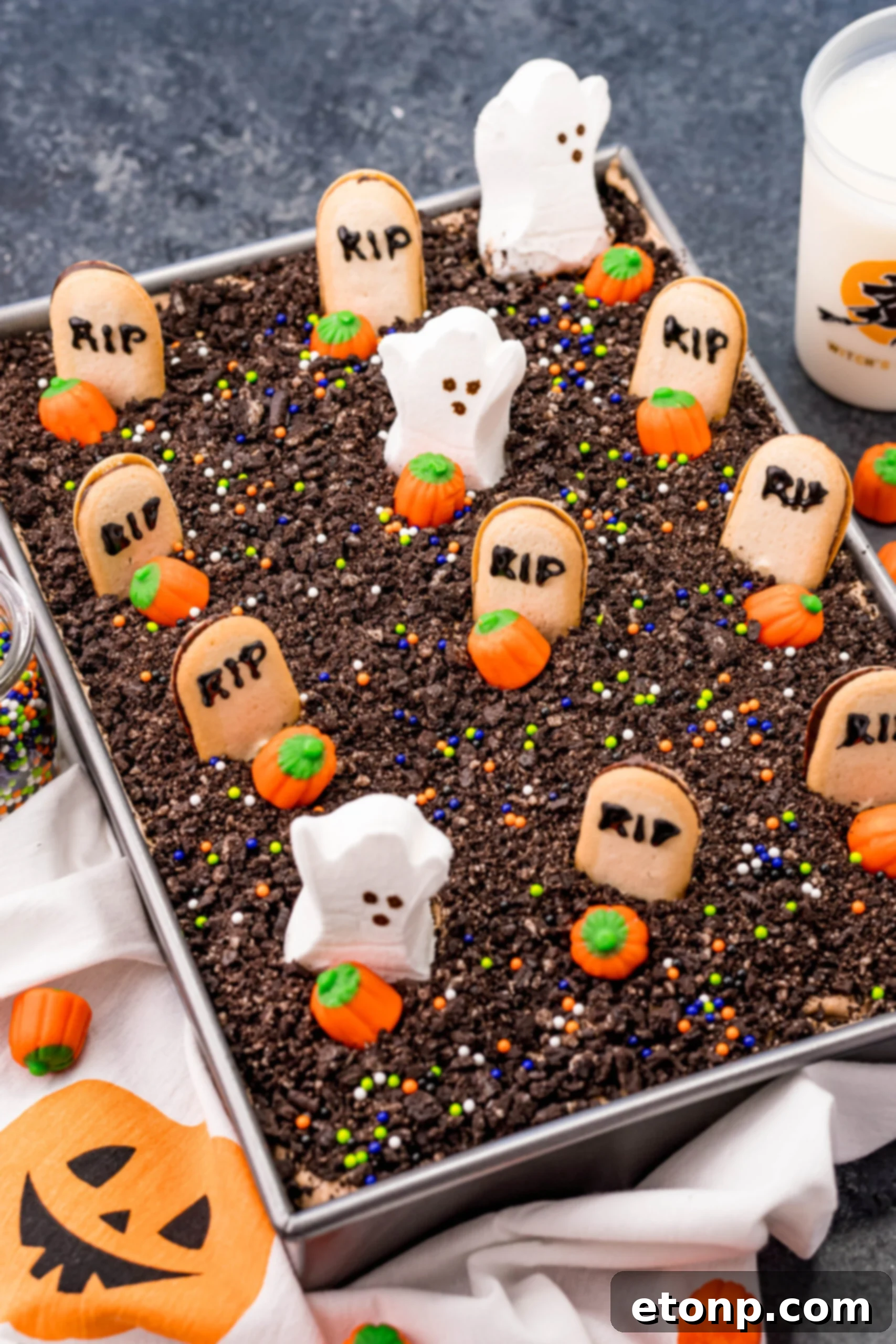 The Halloween Dirt Cake nestled in a silver baking pan, before being cut, showcasing its dark, inviting surface covered with crushed Oreos and festive decorations.