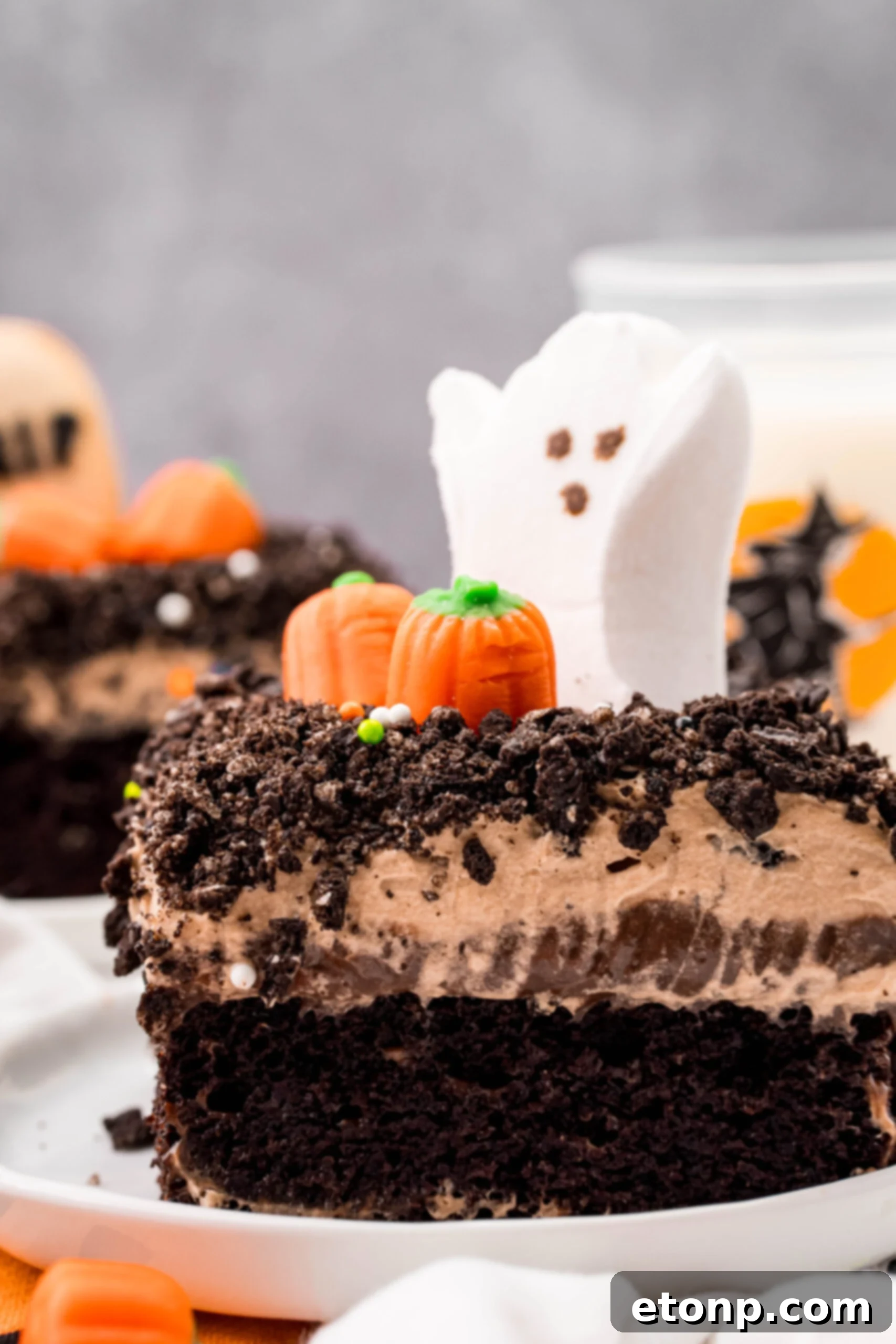 A close-up of a Halloween Dirt Cake slice on a white plate, topped with a ghost marshmallow peep and crushed Oreo crumbles.