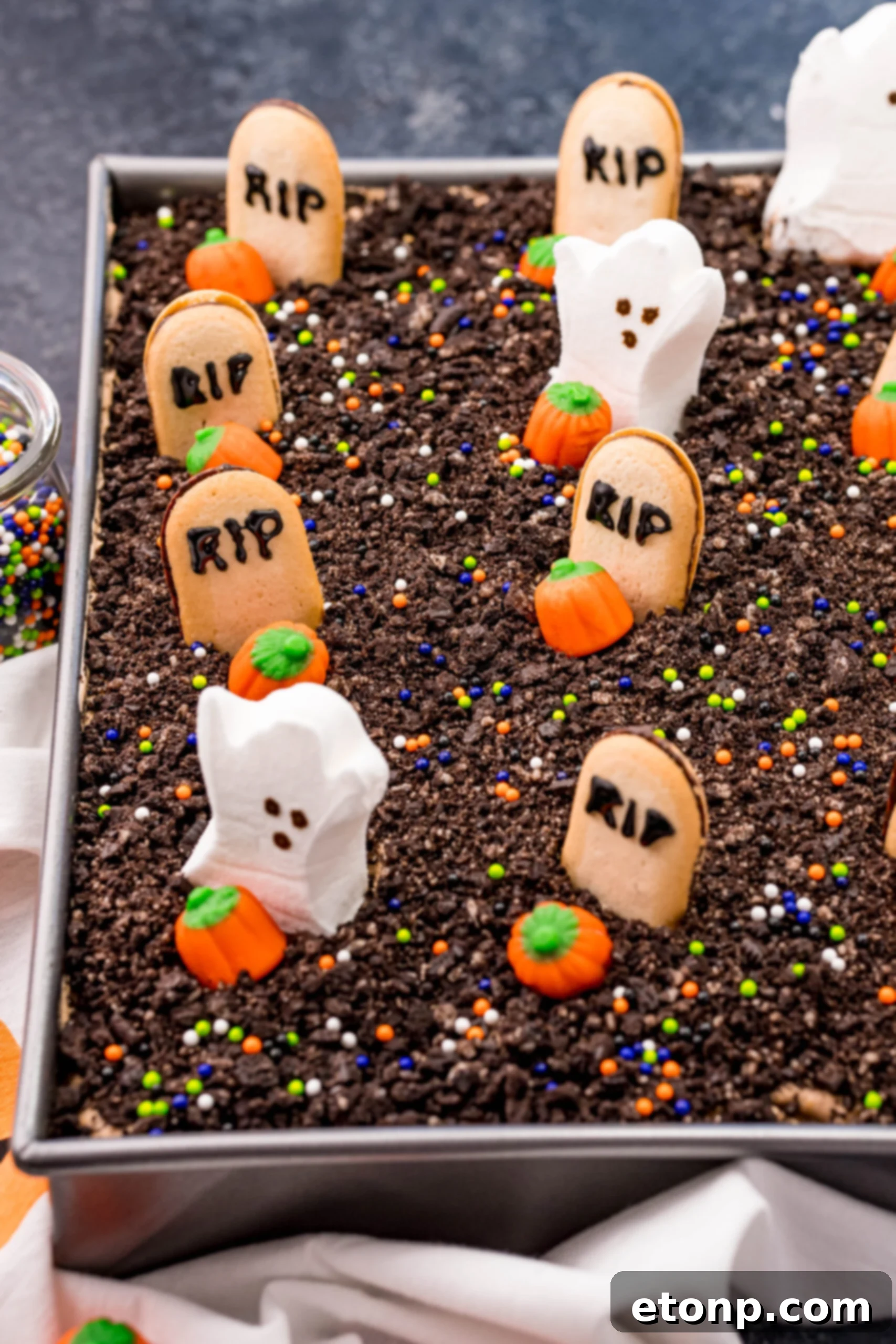 A Halloween Dirt Cake in a silver baking pan, uncut, with its surface covered in crushed Oreos and various Halloween candies like ghost marshmallows and candy pumpkins.