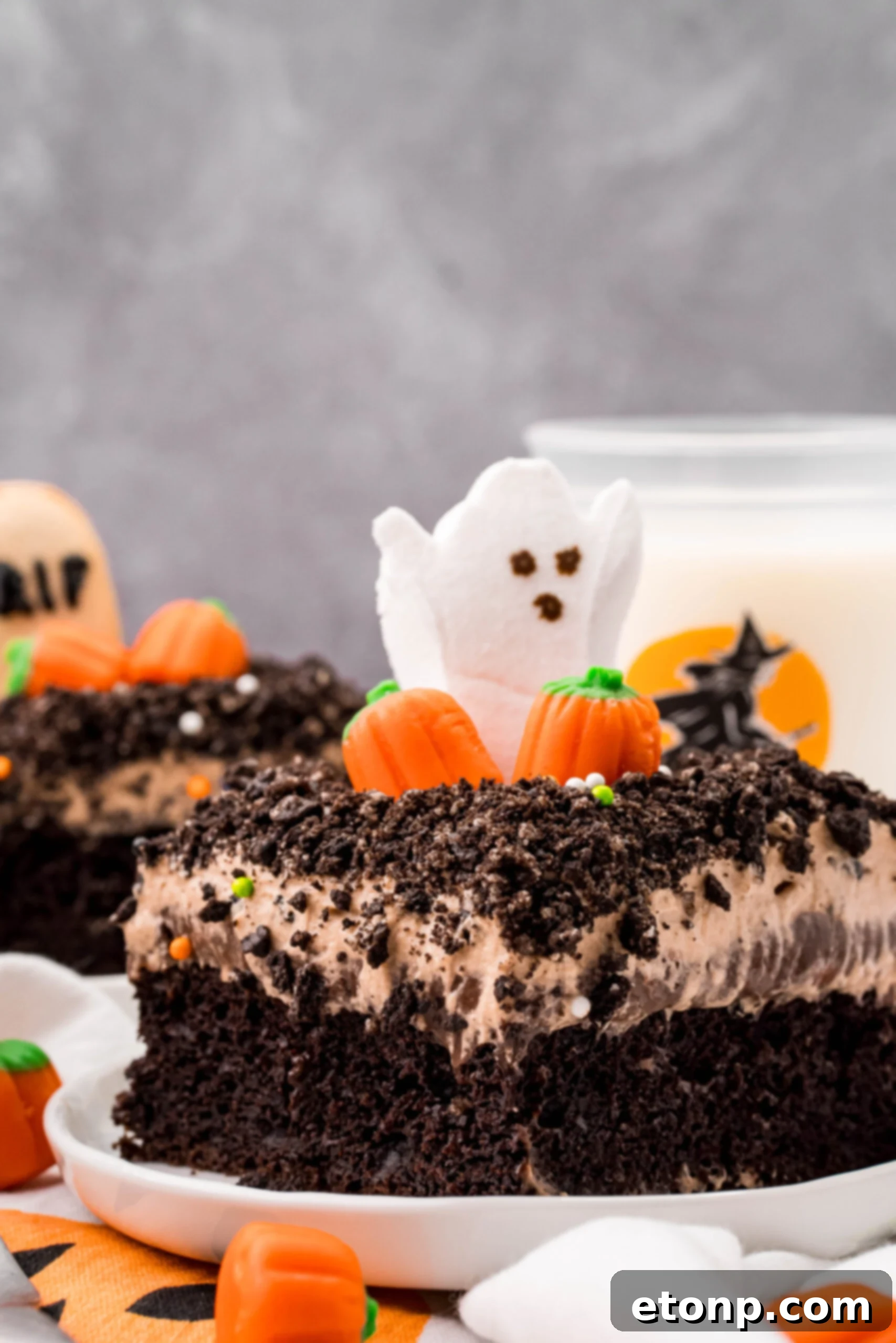A tempting slice of Halloween Dirt Cake on a white plate, with a glass of milk in the blurred background, suggesting a delightful treat.