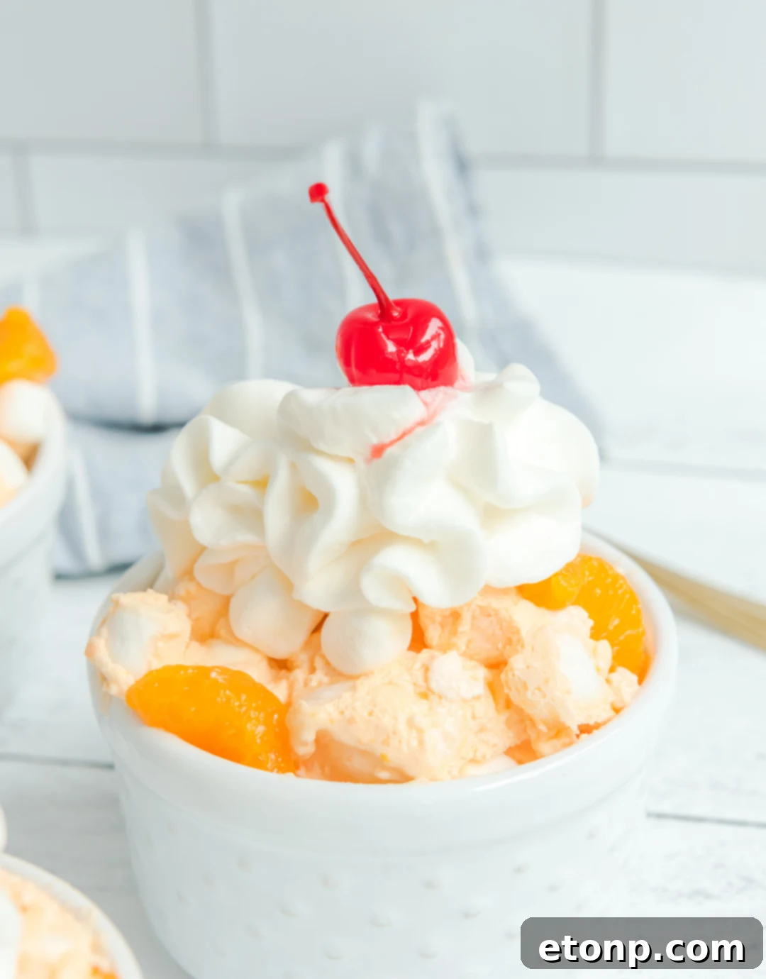 Orange Creamsicle Salad in a white bowl topped with whipped topping and a cherry, ready to be enjoyed.
